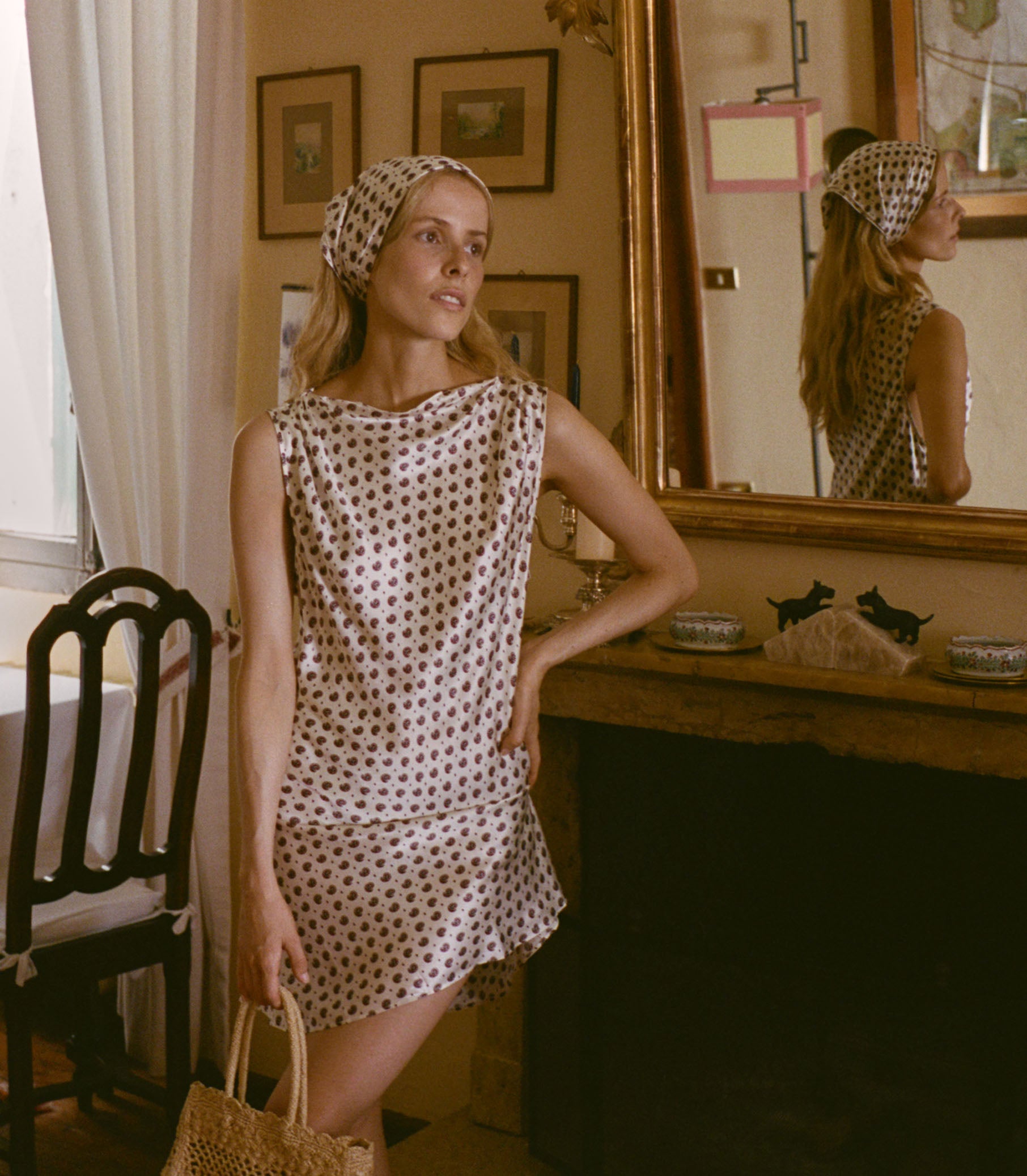 Woman in a print dress standing in a room with a mirror and decor. 6