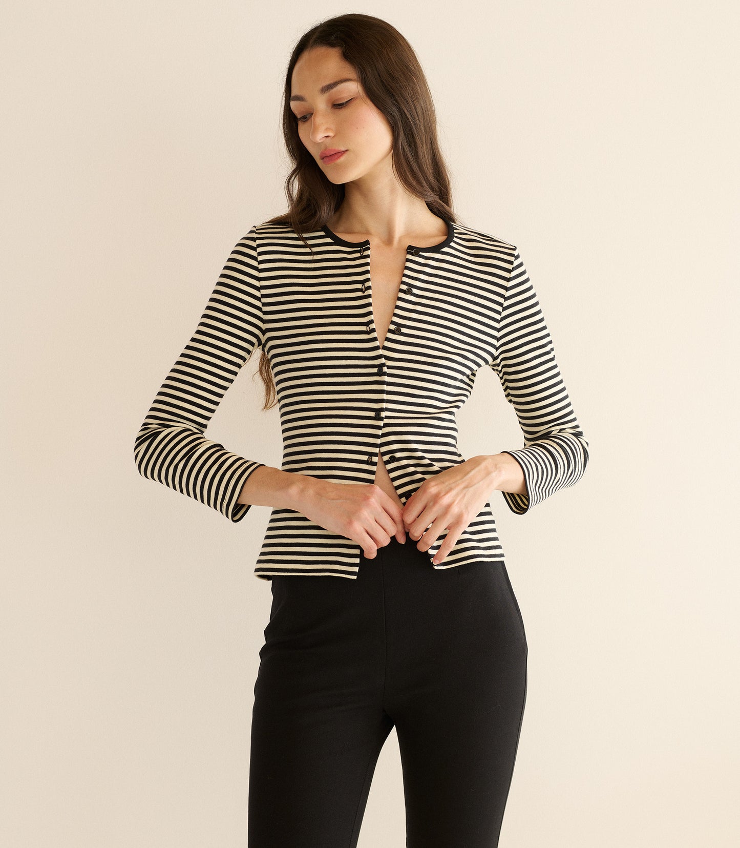 Woman wearing a black and white striped long-sleeve top against a beige background