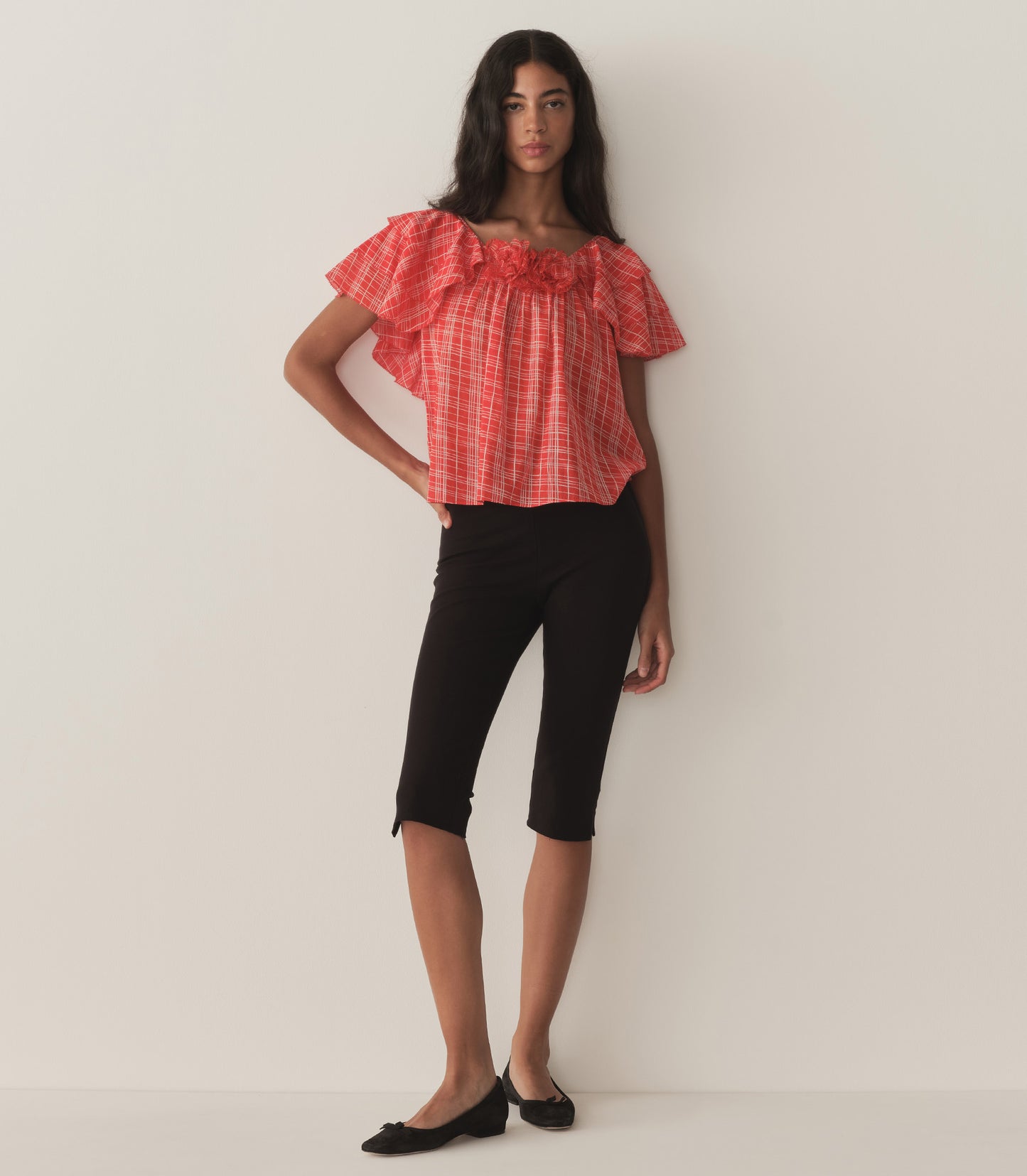 Rocio is wearing a red plaid top with ruffled sleeves, paired with black capris.