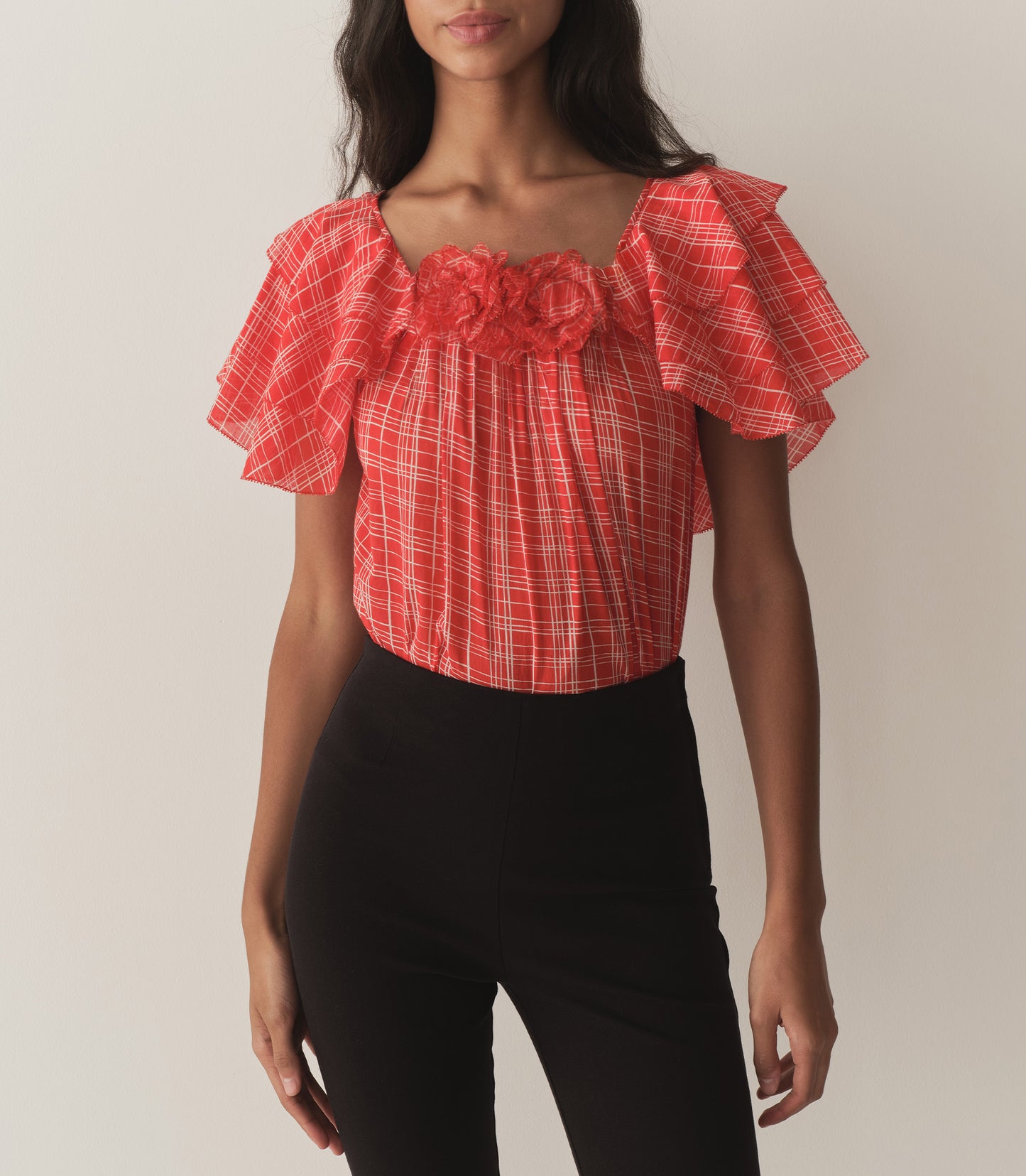 Rocio is wearing a red plaid top with ruffled sleeves, paired with black capris.