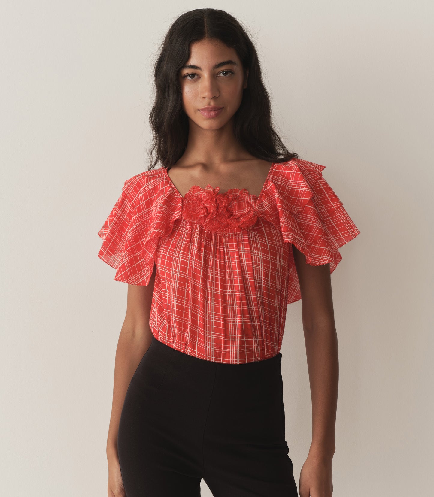 Rocio is wearing a red plaid top with ruffled sleeves, paired with black capris.