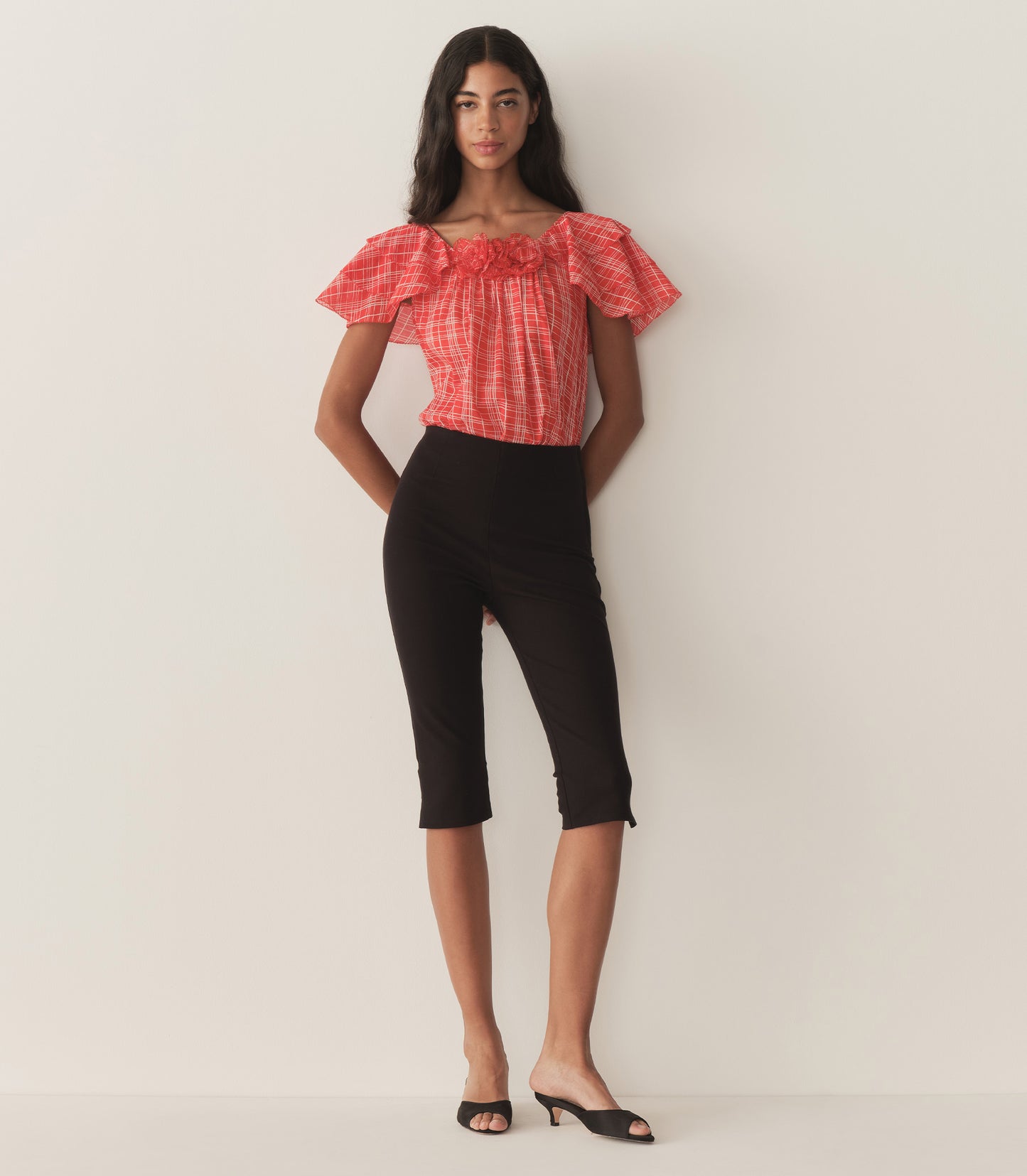 Rocio is wearing a red plaid top with ruffled sleeves, paired with black capris.
