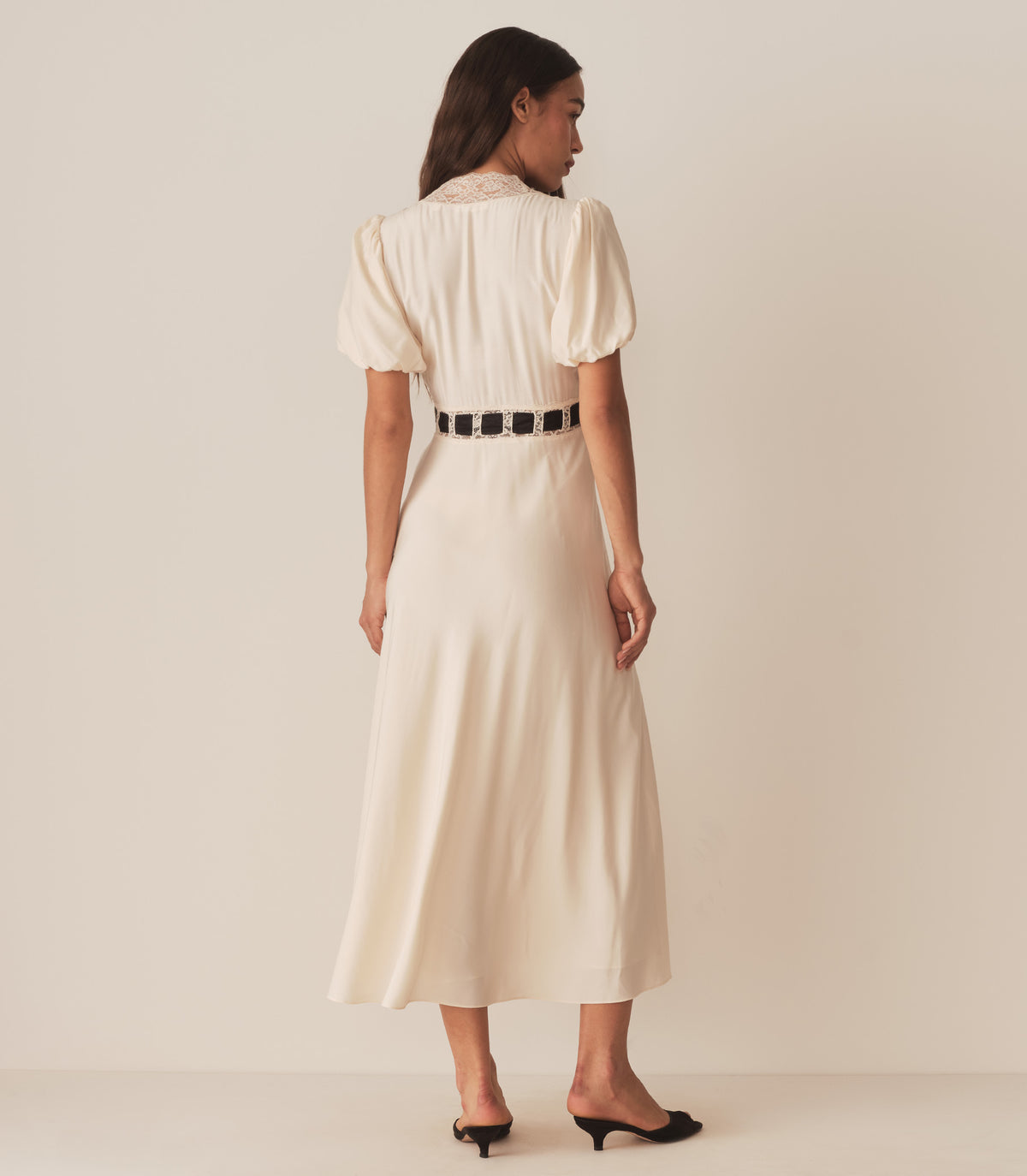 Zahara wears the Augustina Dress in Candlelight, which features short puffed sleeves and a deep V-neckline trimmed with intricate lace.