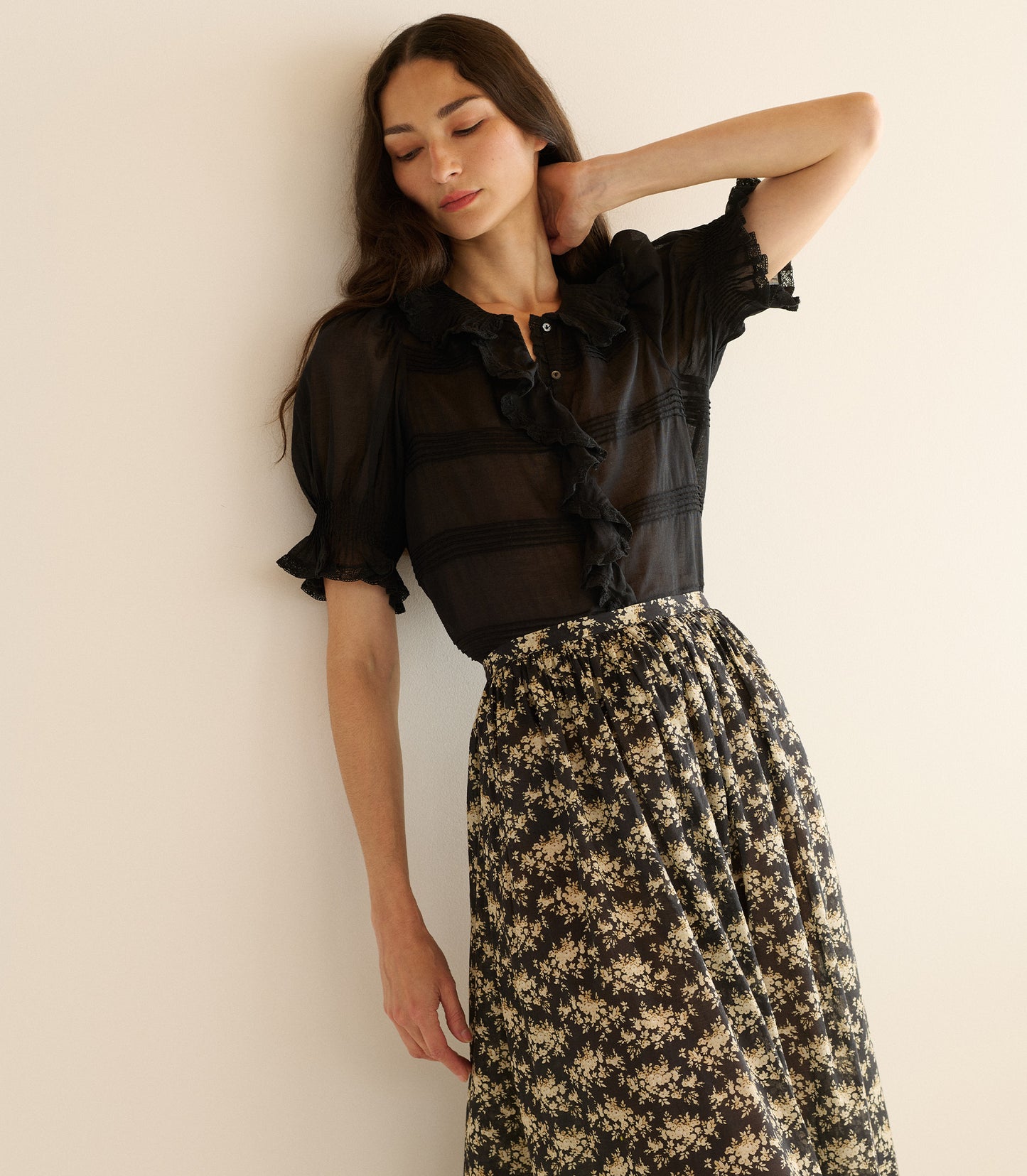 Woman wearing a black blouse and floral skirt against a beige wall