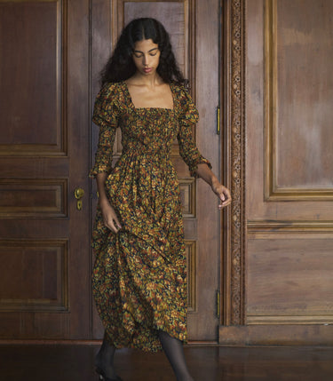 Woman in a floral maxi dress standing in front of a wooden door.