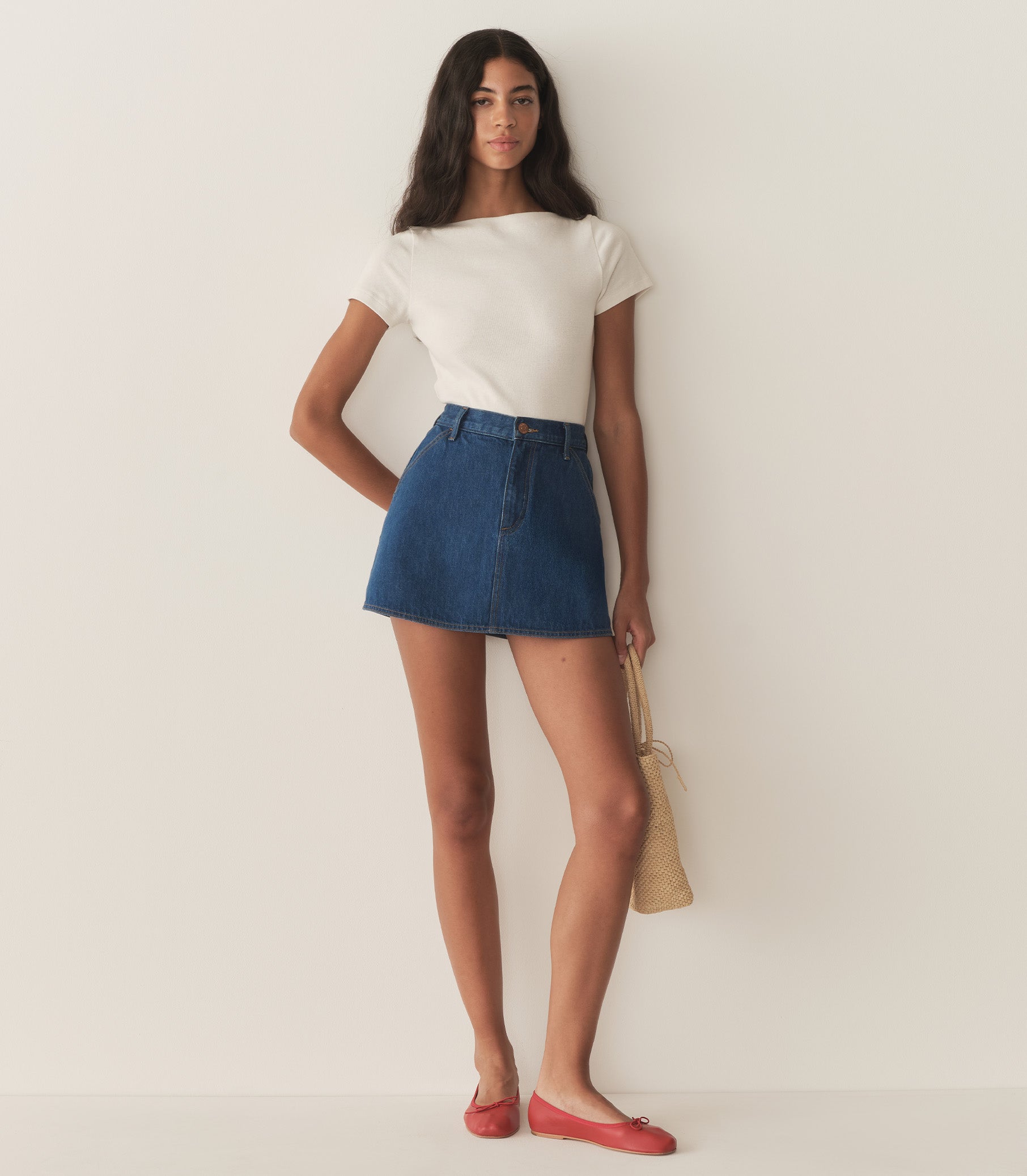 Rocio is wearing a denim A-Line skirt paired with a white top and red flats. 1