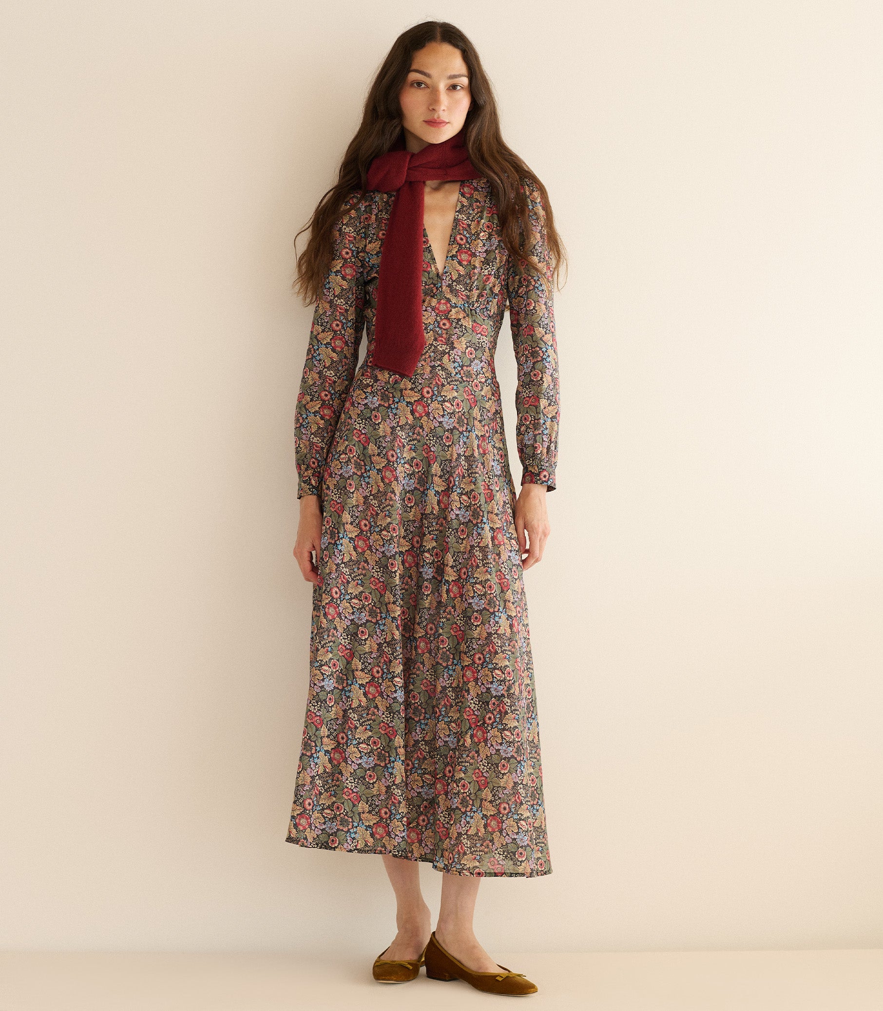 Woman wearing a long floral dress with a red scarf against a plain background 2