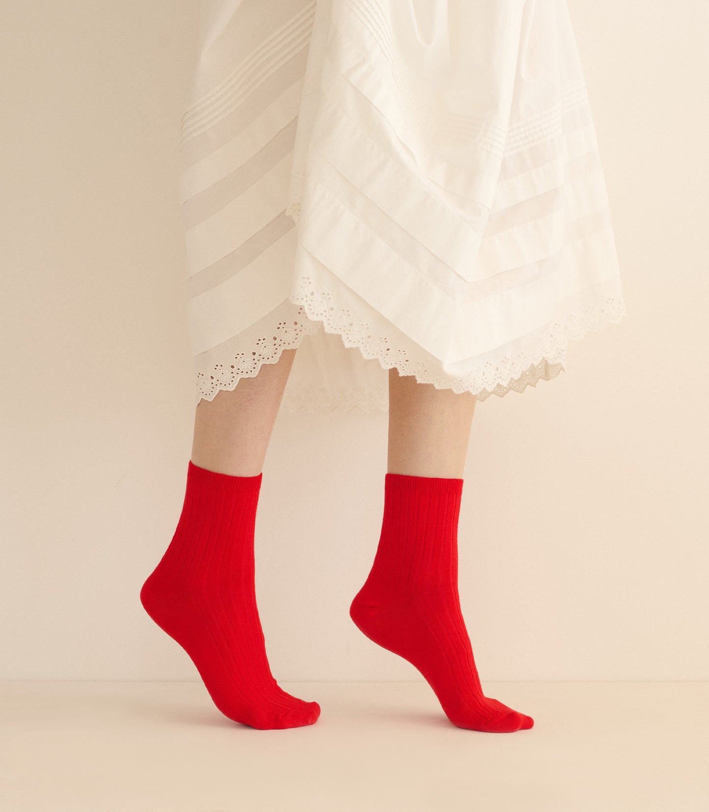 Red socks worn with a white lace dress on a beige background