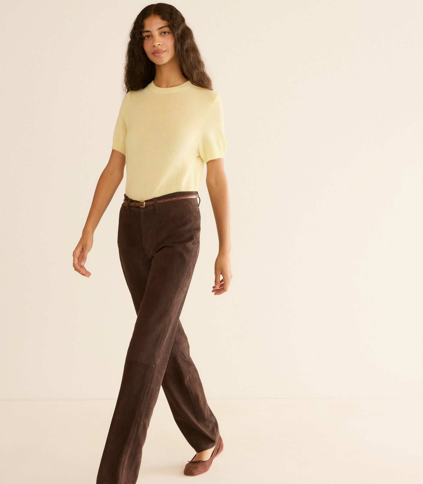 Woman wearing a yellow top and brown pants on a beige background