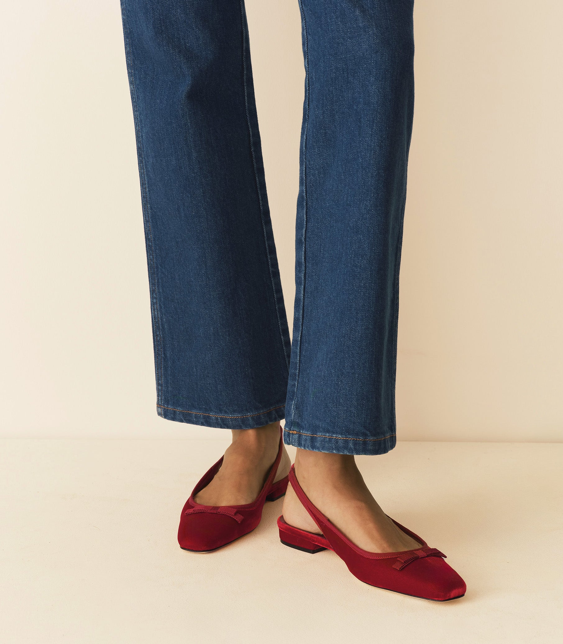 Person wearing blue jeans and red shoes on a beige background