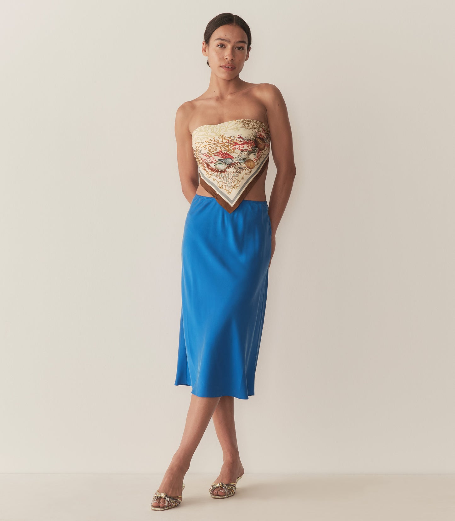 Zahara is wearing a blue midi skirt paired with a bandana top and metallic kitten heels.