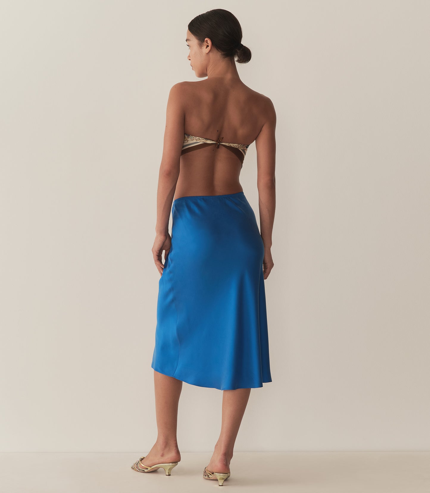 Zahara is wearing a blue midi skirt paired with a bandana top and metallic kitten heels.