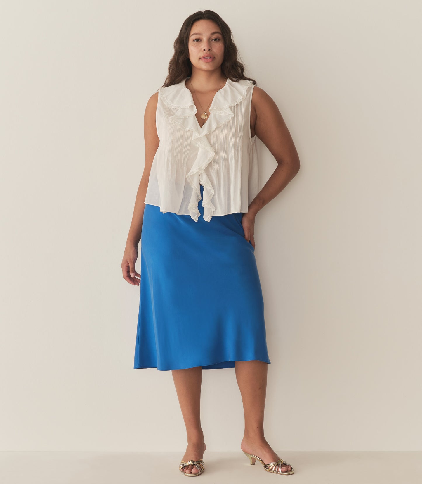 Alana is wearing a blue midi skirt paired with a white sleeveless top and metallic kitten heels.