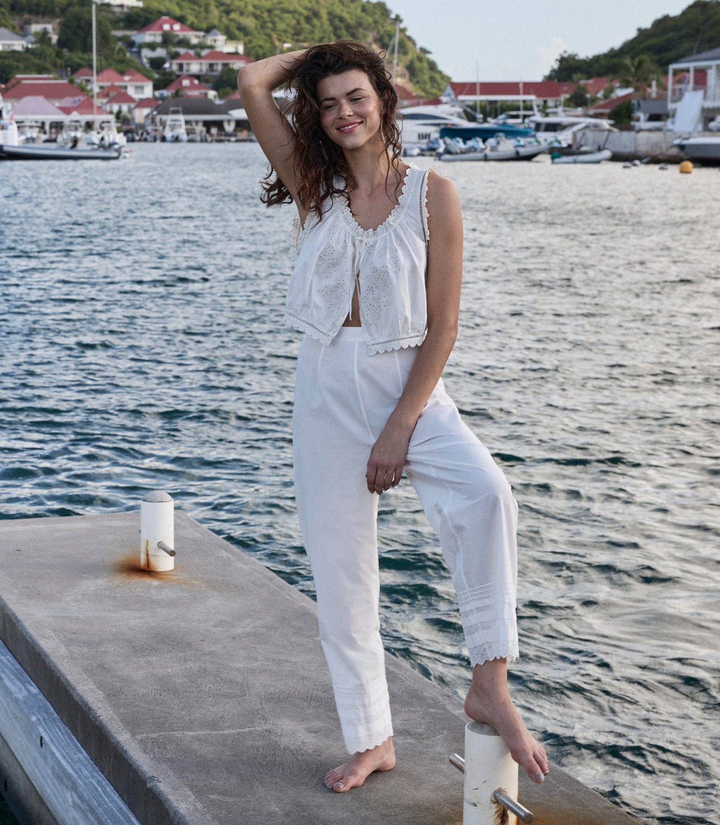 Georgia is wearing white pants and a white blouse in front of a lake.