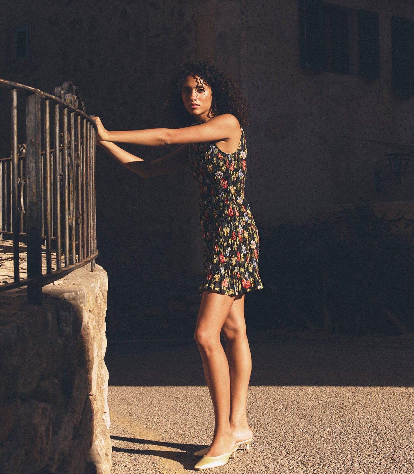 Melodie is wearing a black floral mini dress in front of a rustic background.