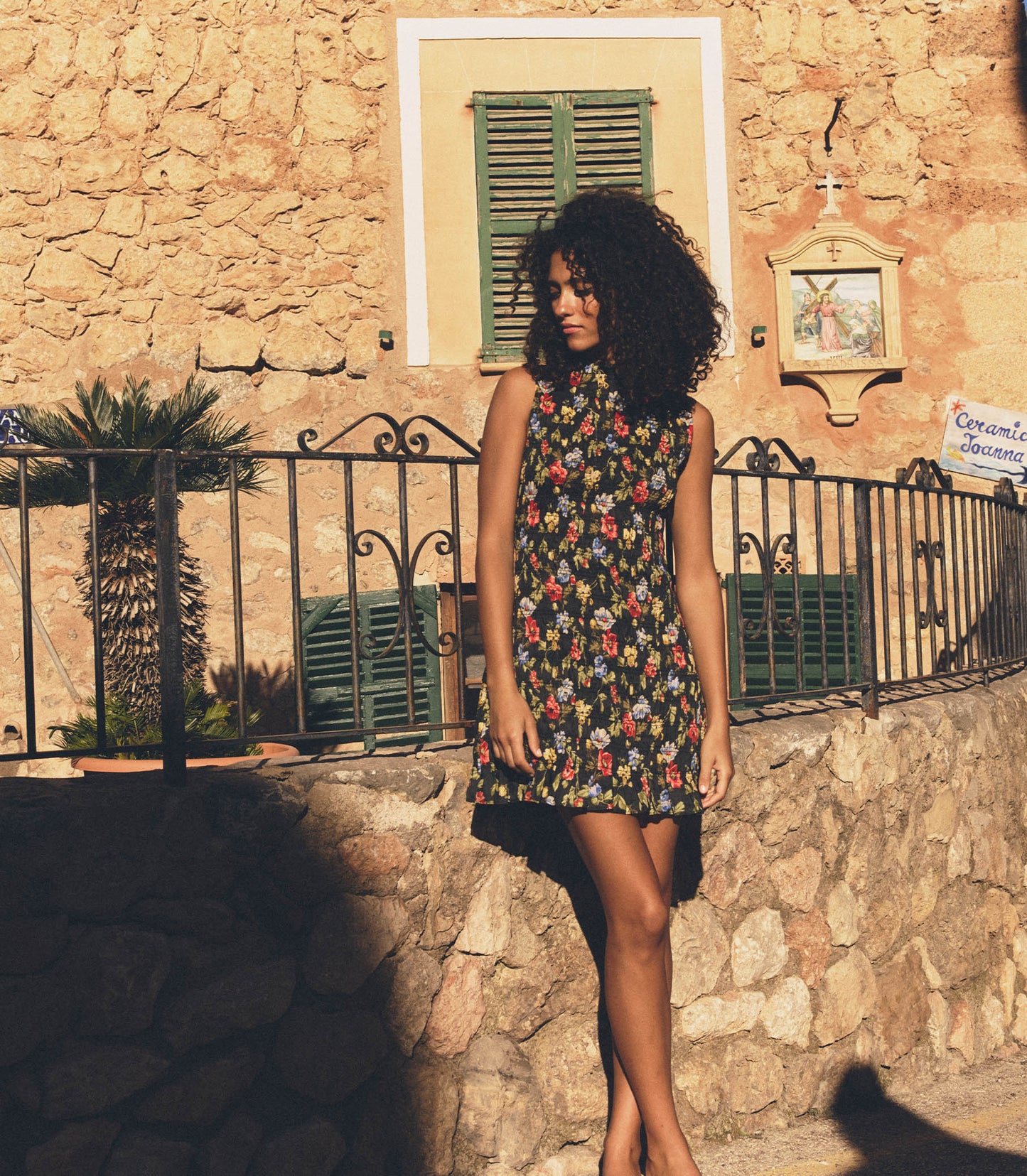 Melodie is wearing a black floral mini dress in front of a rustic background.