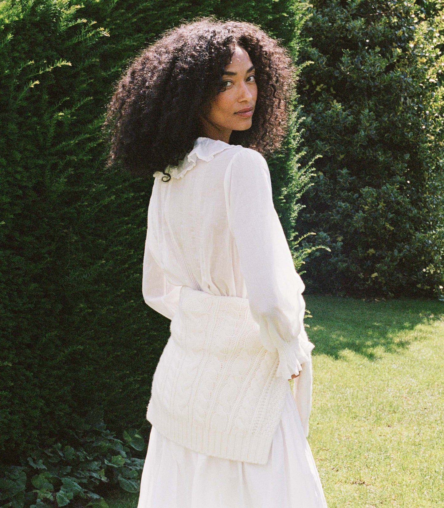 Woman wearing a white blouse and white skirt amongst greenery