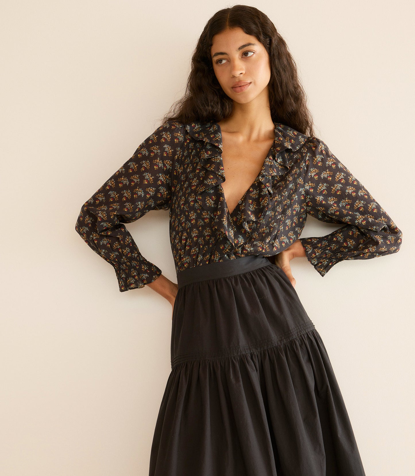 Woman wearing a floral blouse and black skirt against a beige wall