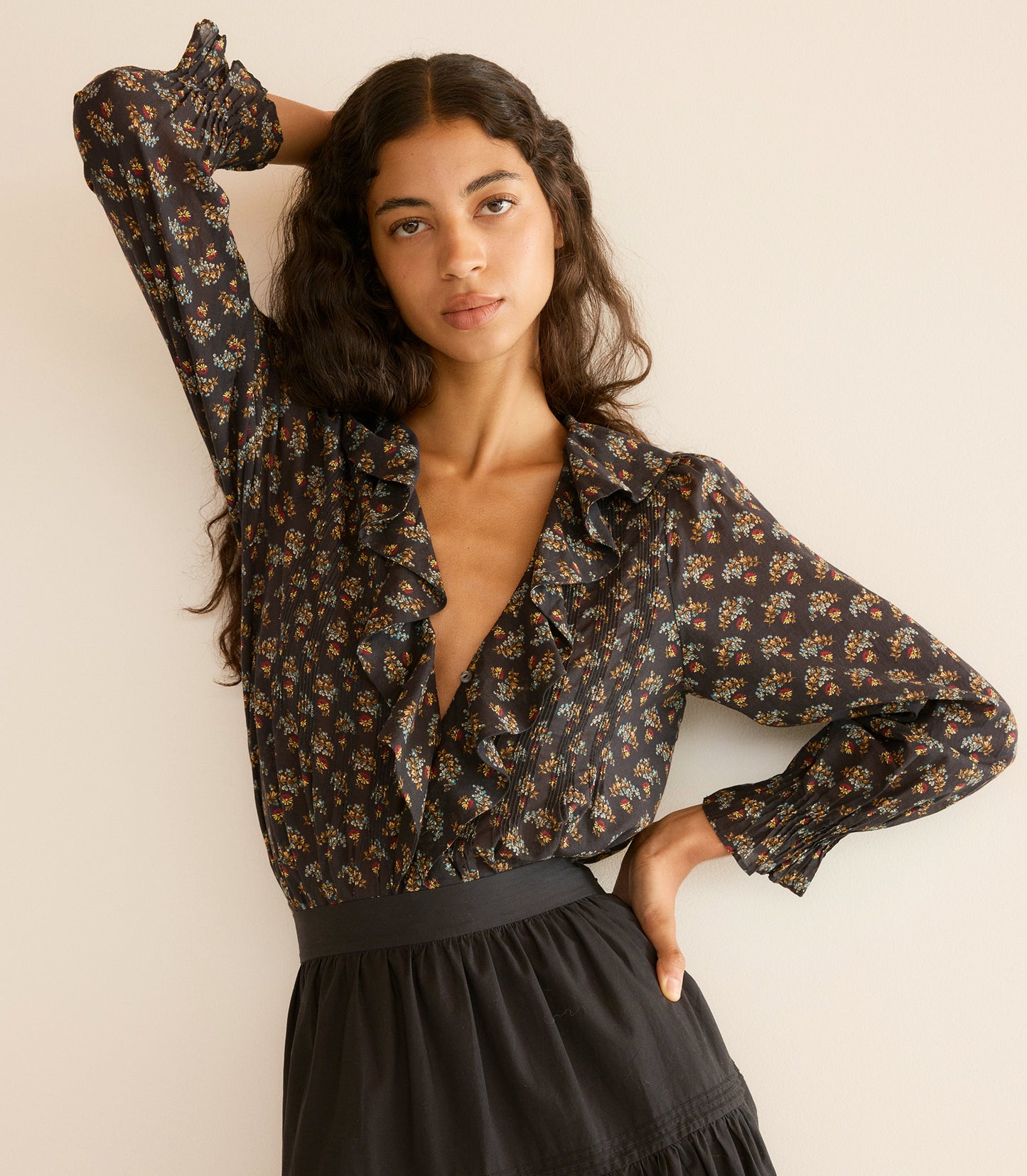 Woman wearing a floral blouse and black skirt against a plain background