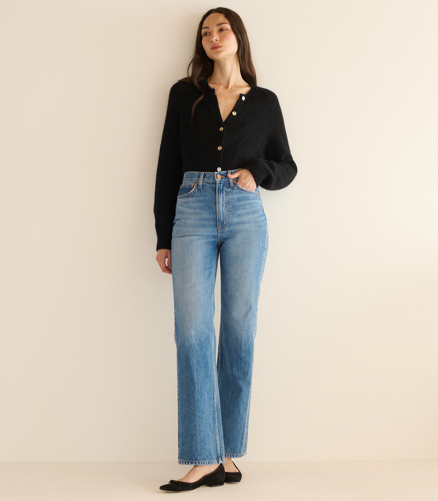 Woman wearing a black cardigan and blue jeans on a beige background