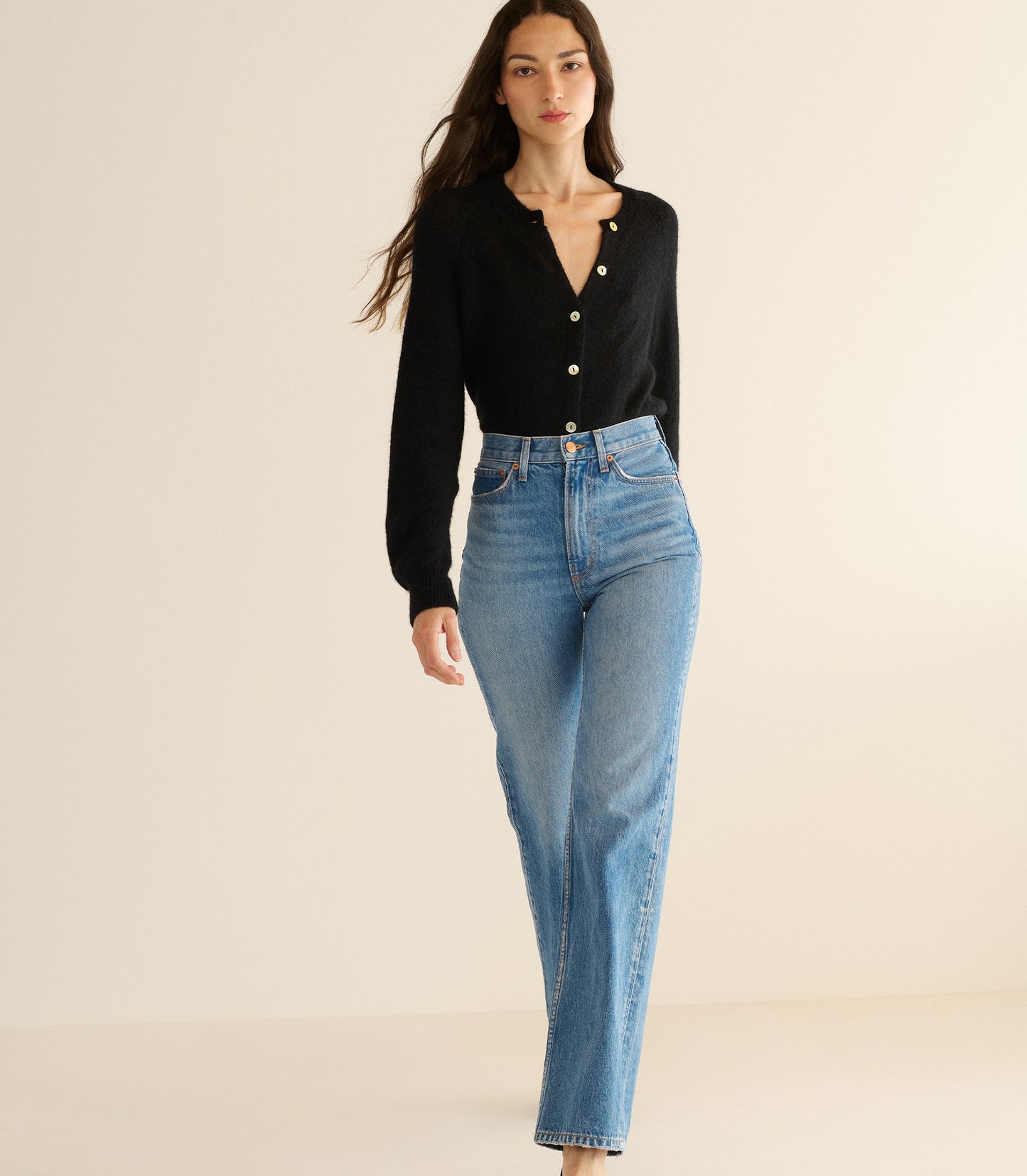 Woman wearing a black cardigan and blue jeans on a beige background