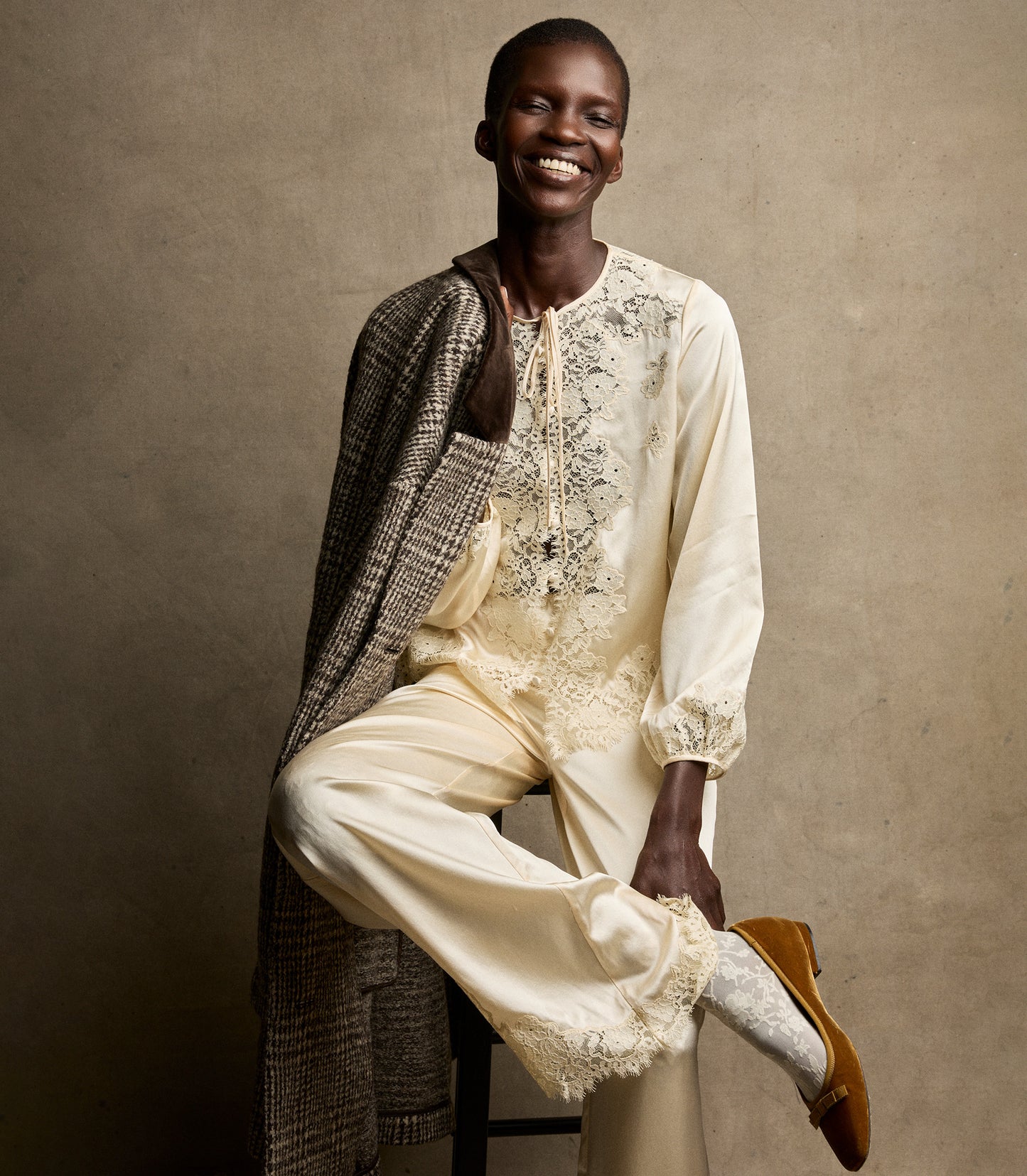 Person wearing a cream-colored outfit with intricate lace against a beige background