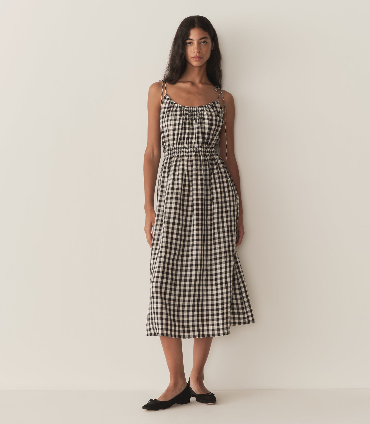 Rocio is wearing a mid-length black and white gingham dress with black flats.