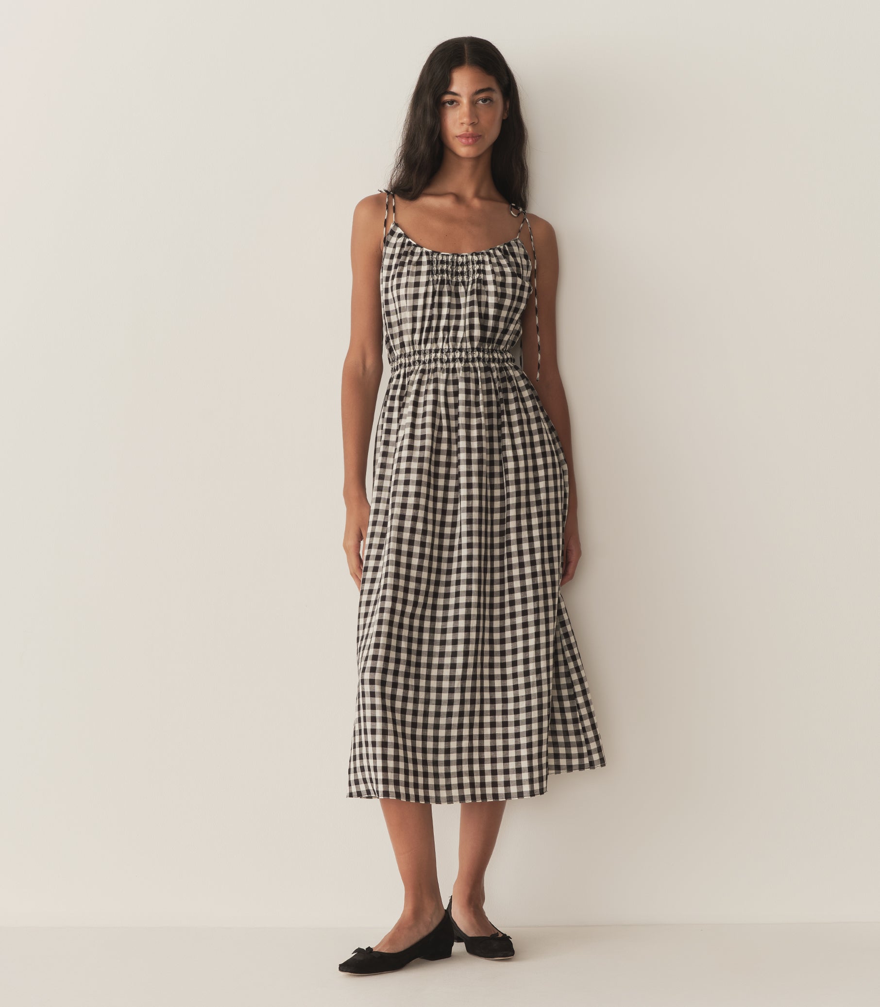 Rocio is wearing a mid-length black and white gingham dress with black flats.