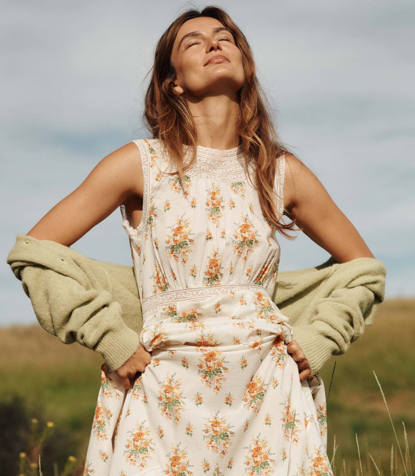 Woman in a floral dress with a green cardigan standing in a field