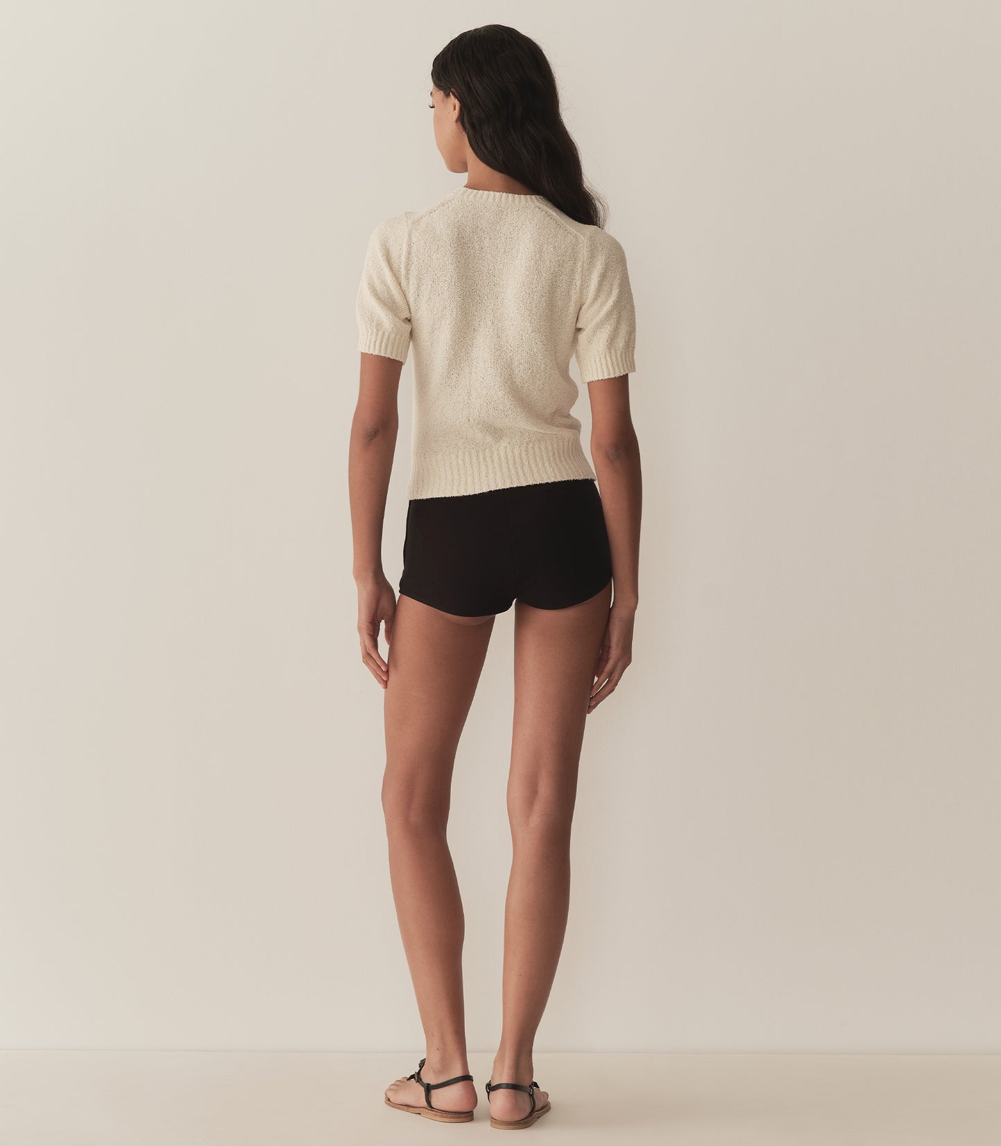 Rocio is wearing a sand colored short sleeve sweater paired with black micro shorts.
