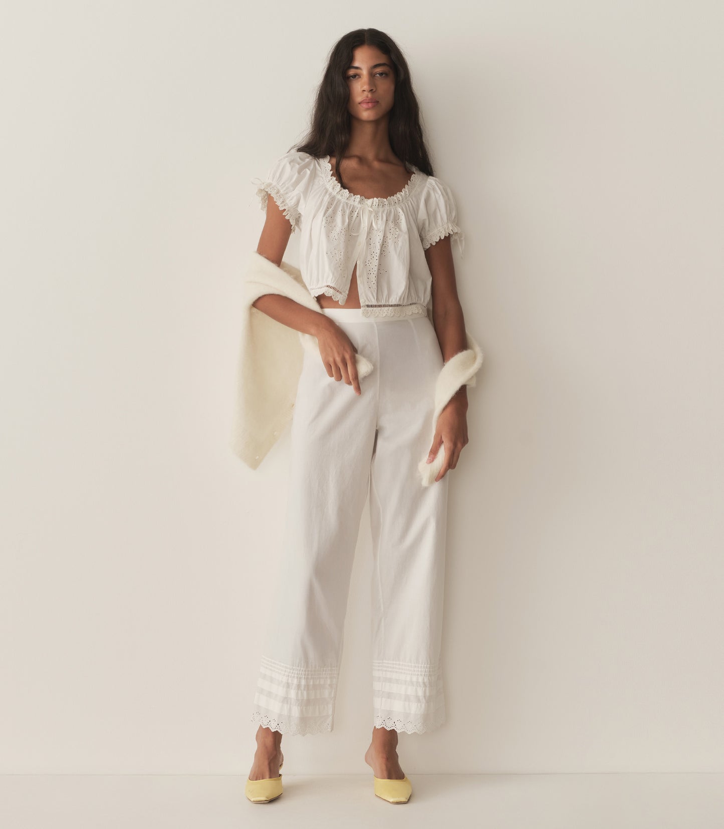 Rocio is wearing a white short puff sleeve top with white pants and yellow mule heels.