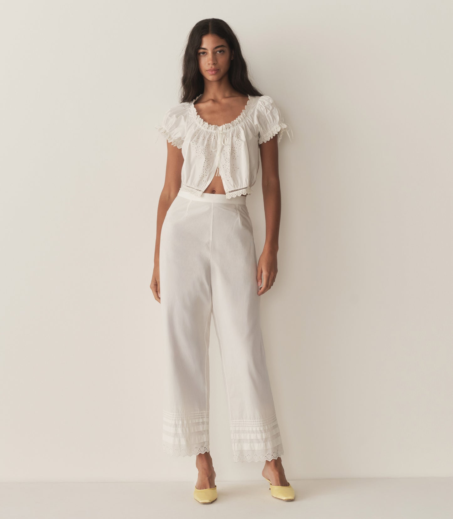 Rocio is wearing a white short puff sleeve top with white pants and yellow mule heels.