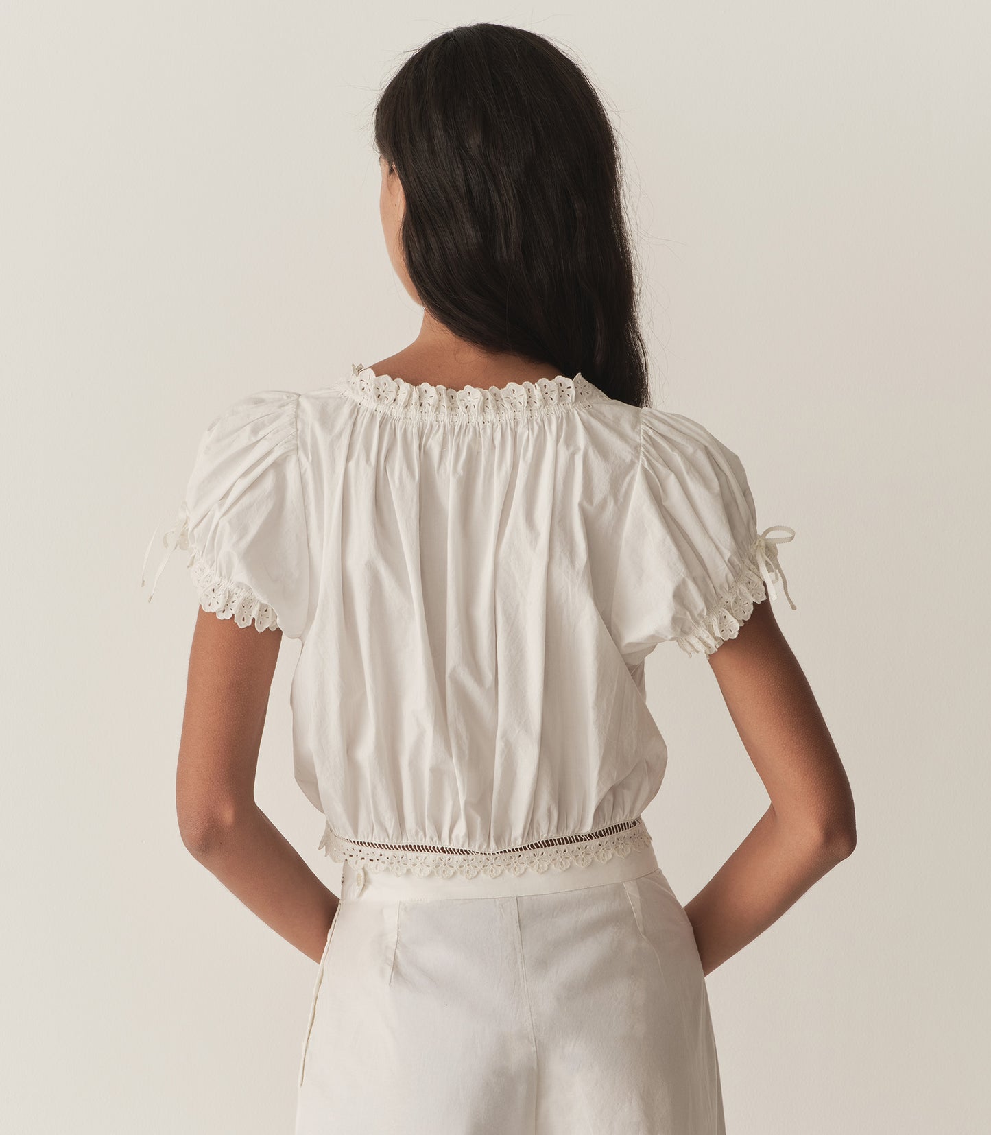 Rocio is wearing a white short puff sleeve top with white pants and yellow mule heels.