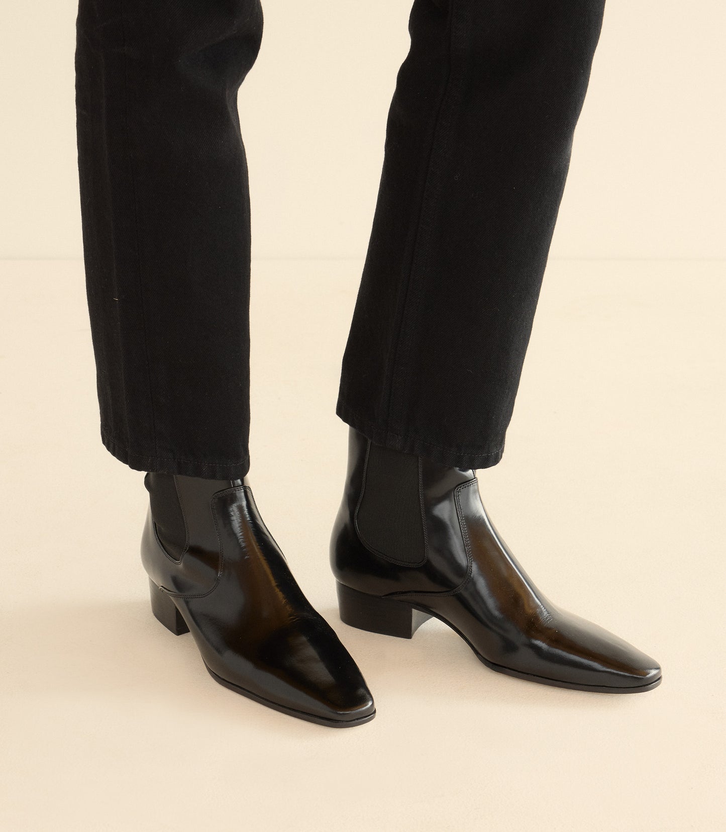 Black patent leather shoes worn with black pants on a beige background