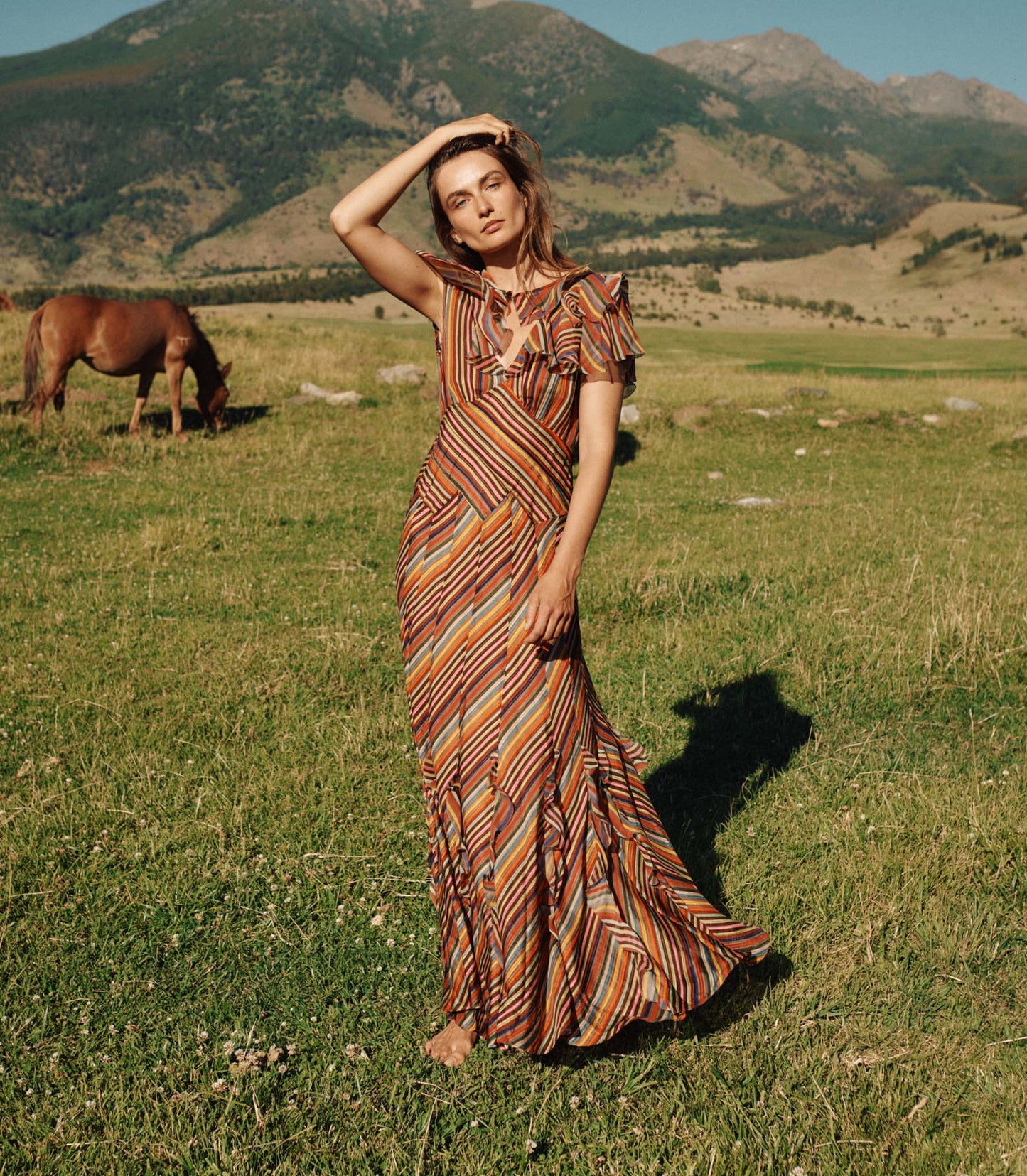 Woman in a striped dress standing in a field with mountains in the background
