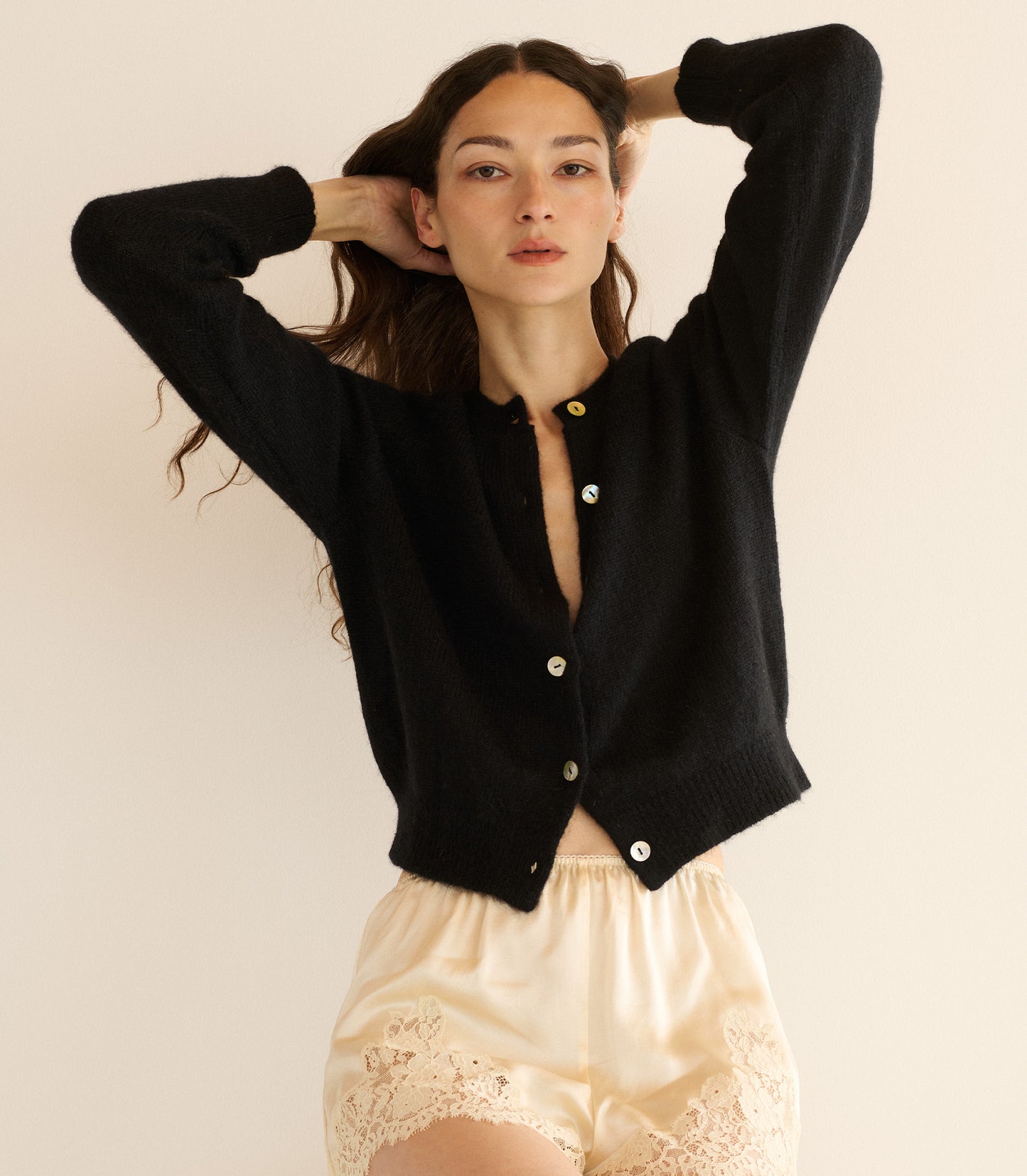Woman wearing a black cardigan over a beige top with lace details on a plain background