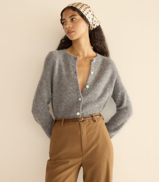 Woman wearing a gray cardigan and brown pants with a beige headband against a plain background