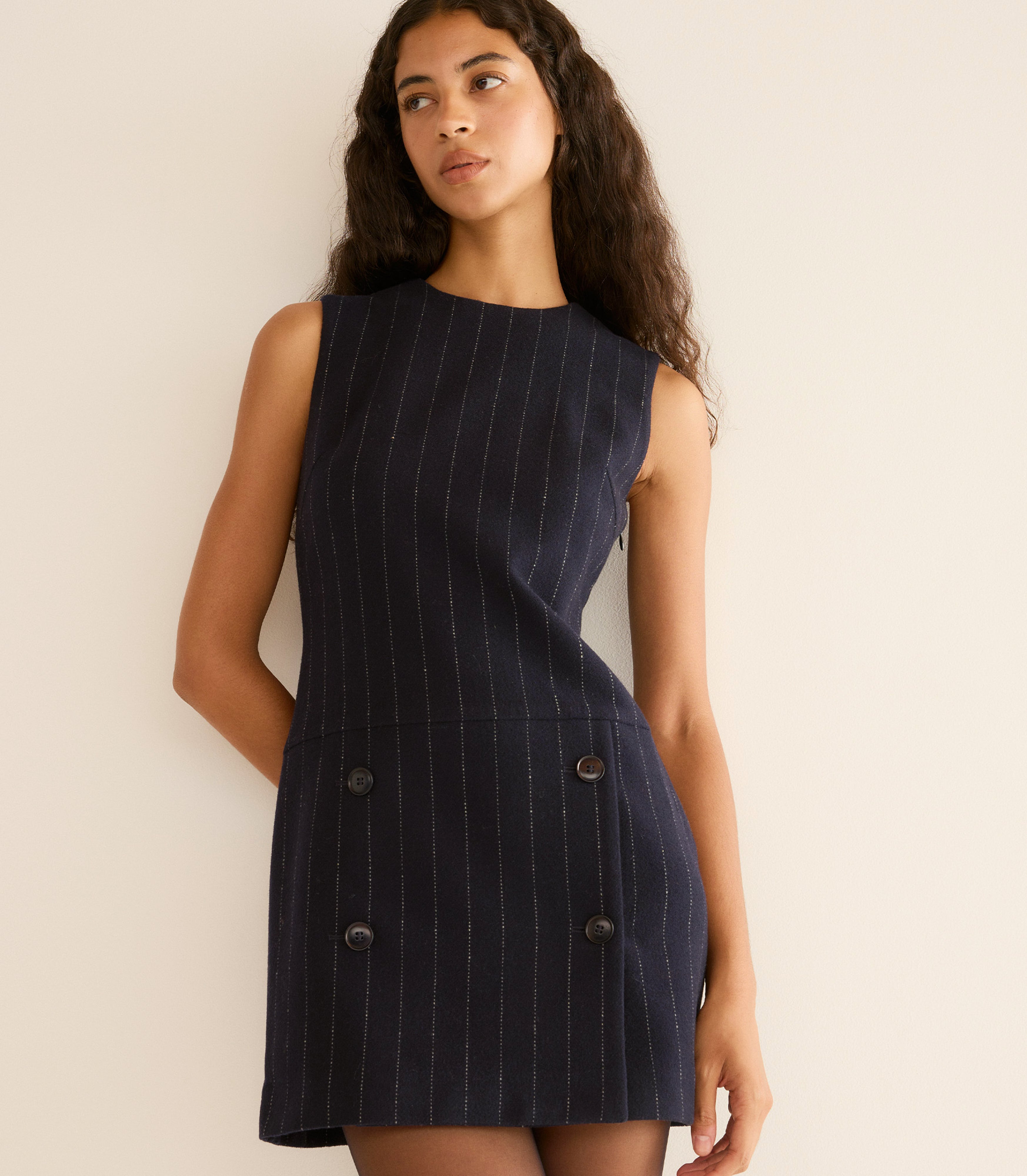 Woman wearing a navy pinstripe dress against a beige background