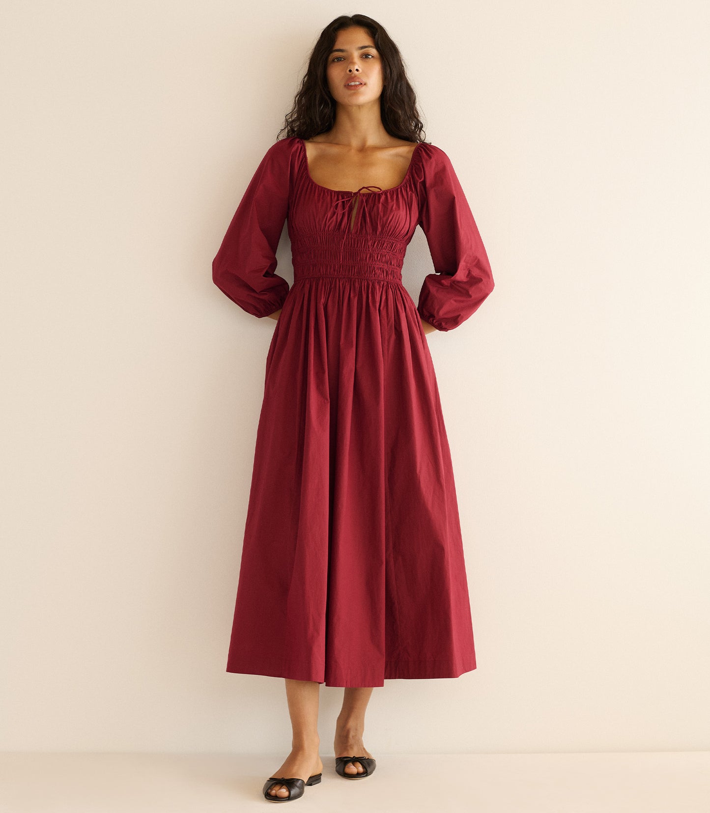 Woman wearing a burgundy dress sitting against a plain background