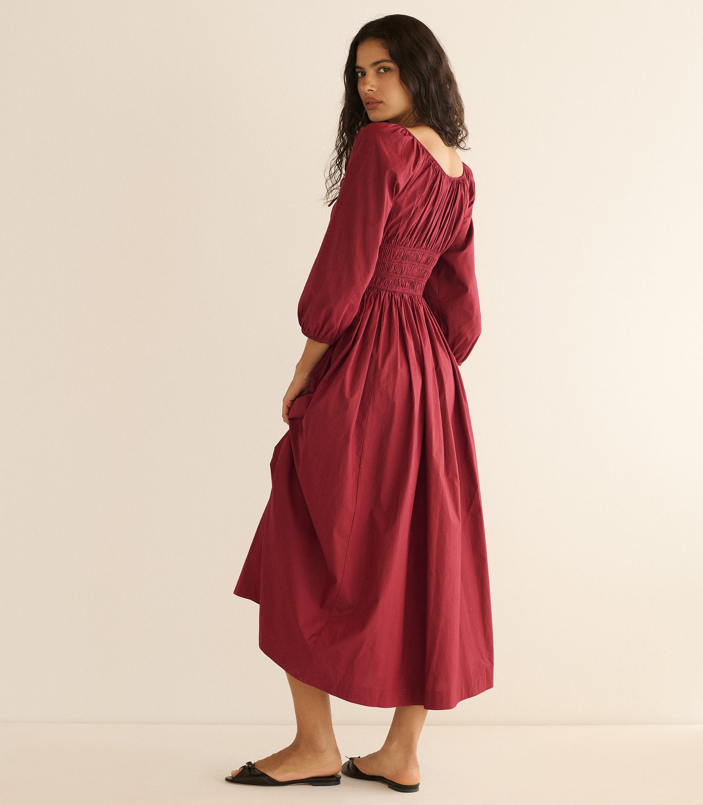 Woman wearing a burgundy dress sitting against a plain background