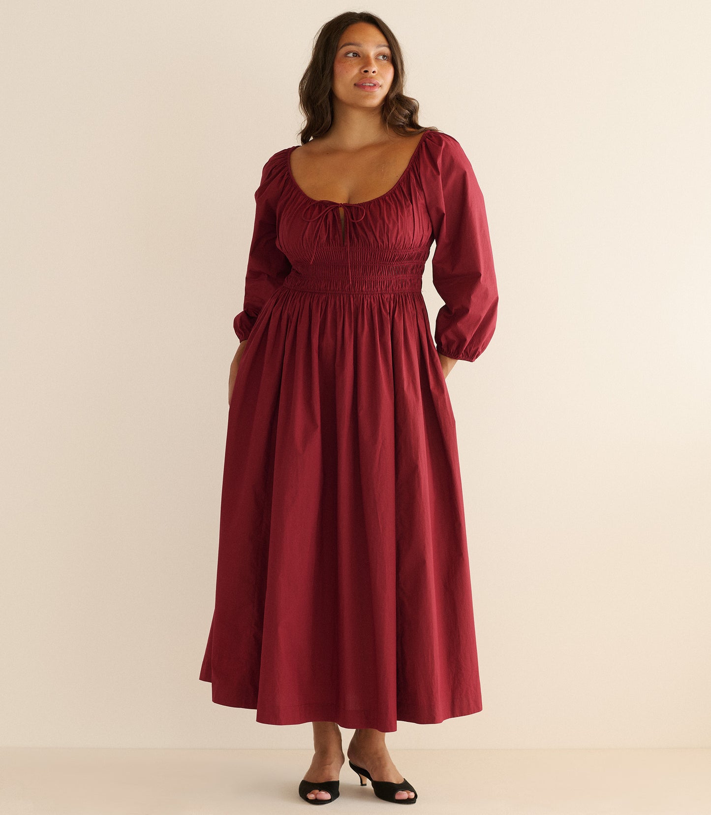 Woman wearing a burgundy dress sitting against a plain background