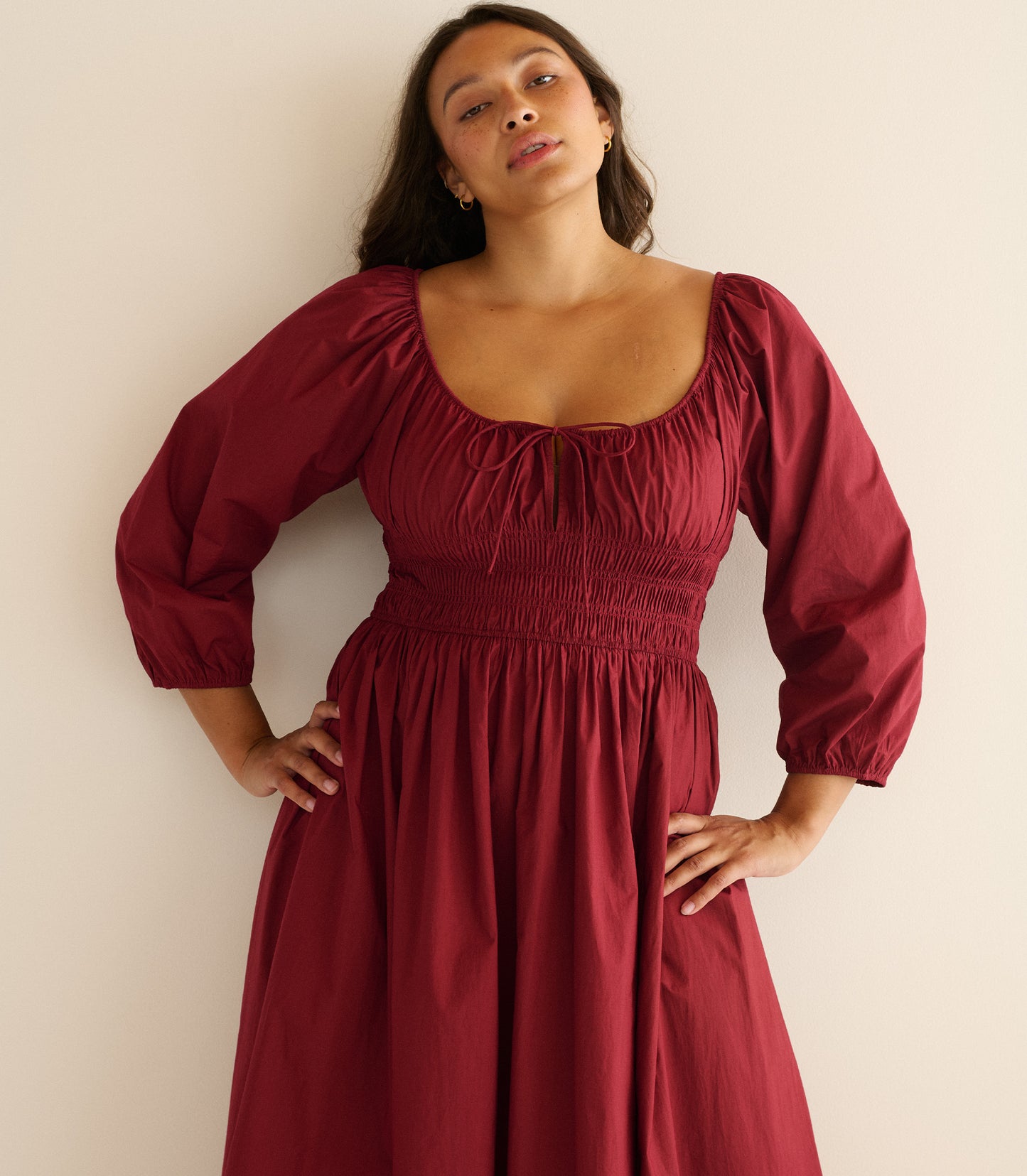 Woman wearing a burgundy dress sitting against a plain background