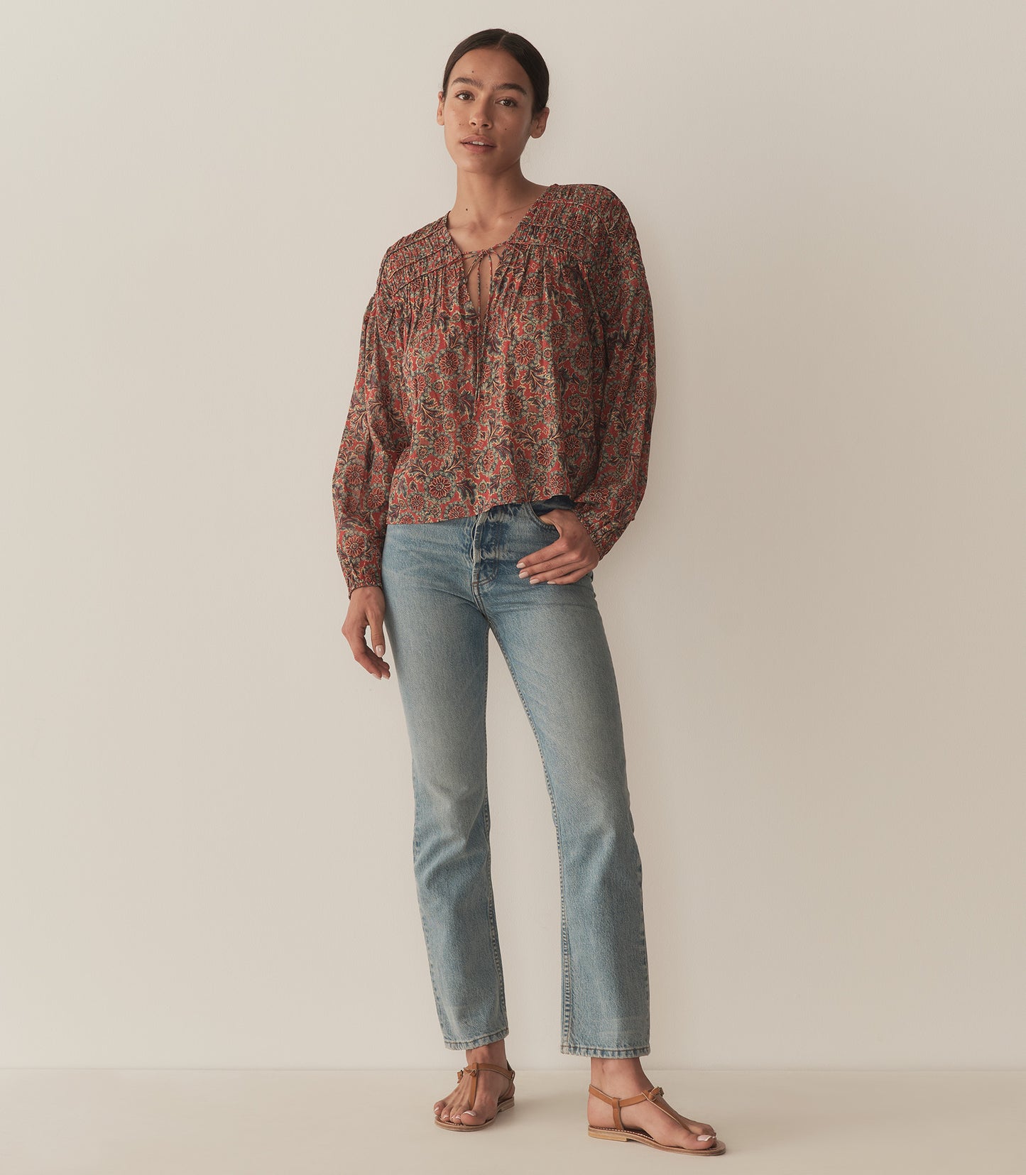 Zahara wears a burnt orange floral blouse fashioned with long balloon sleeves and paired with blue jeans and tan sandals.