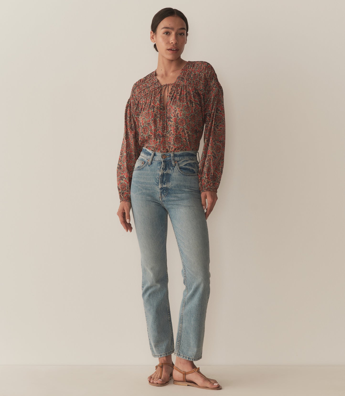 Zahara wears a burnt orange floral blouse fashioned with long balloon sleeves and paired with blue jeans and tan sandals.