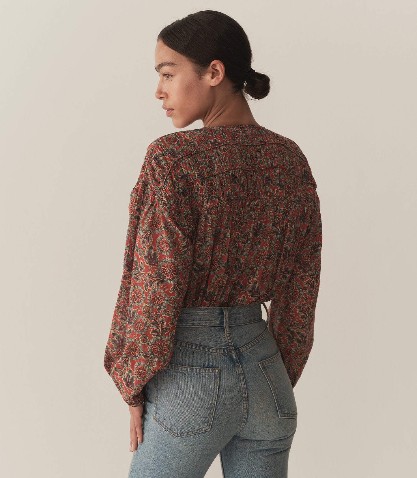 Zahara wears a burnt orange floral blouse fashioned with long balloon sleeves and paired with blue jeans and tan sandals.