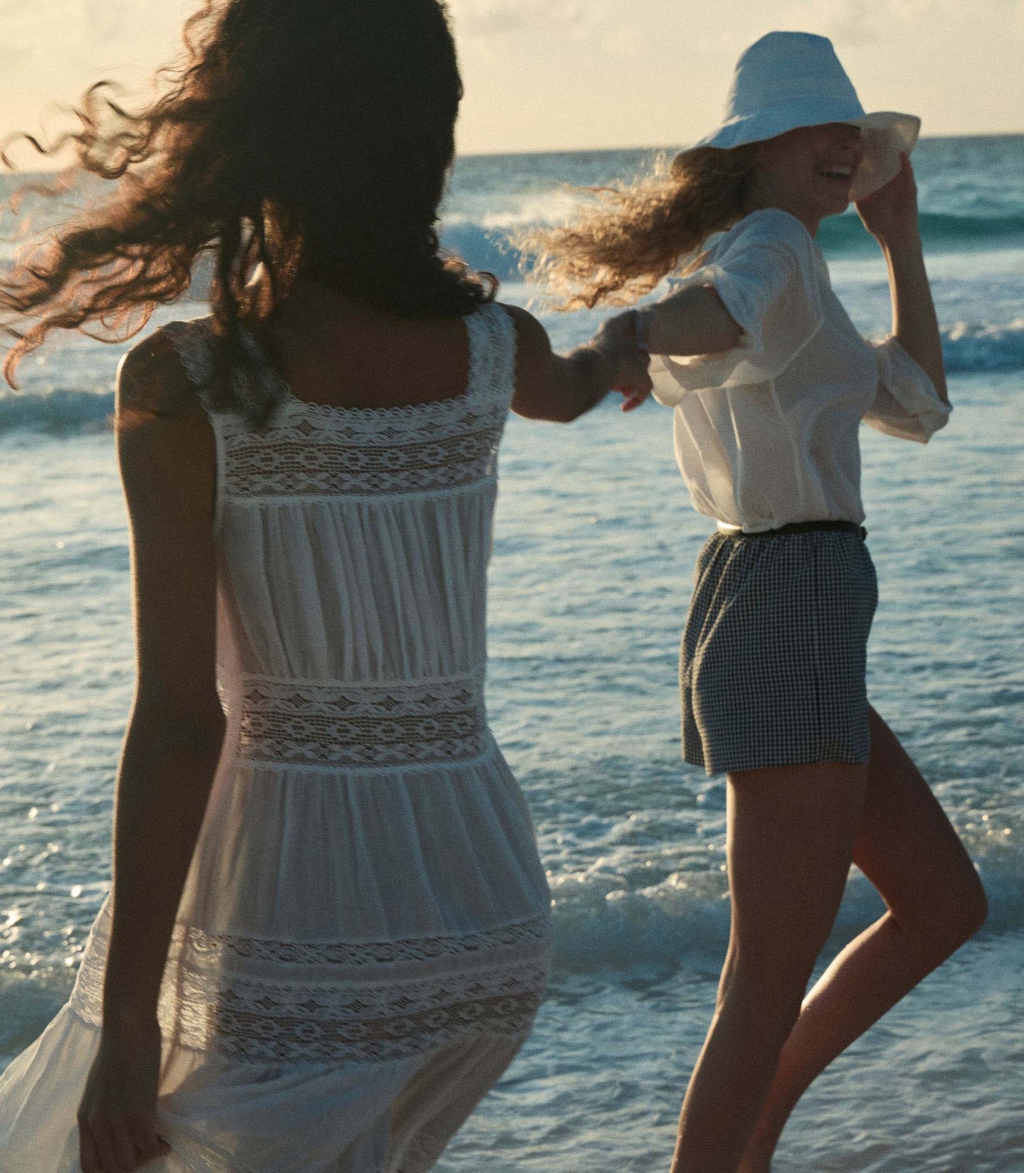 Rocio is wearing a long white sleeveless dress as she walks through the beach.