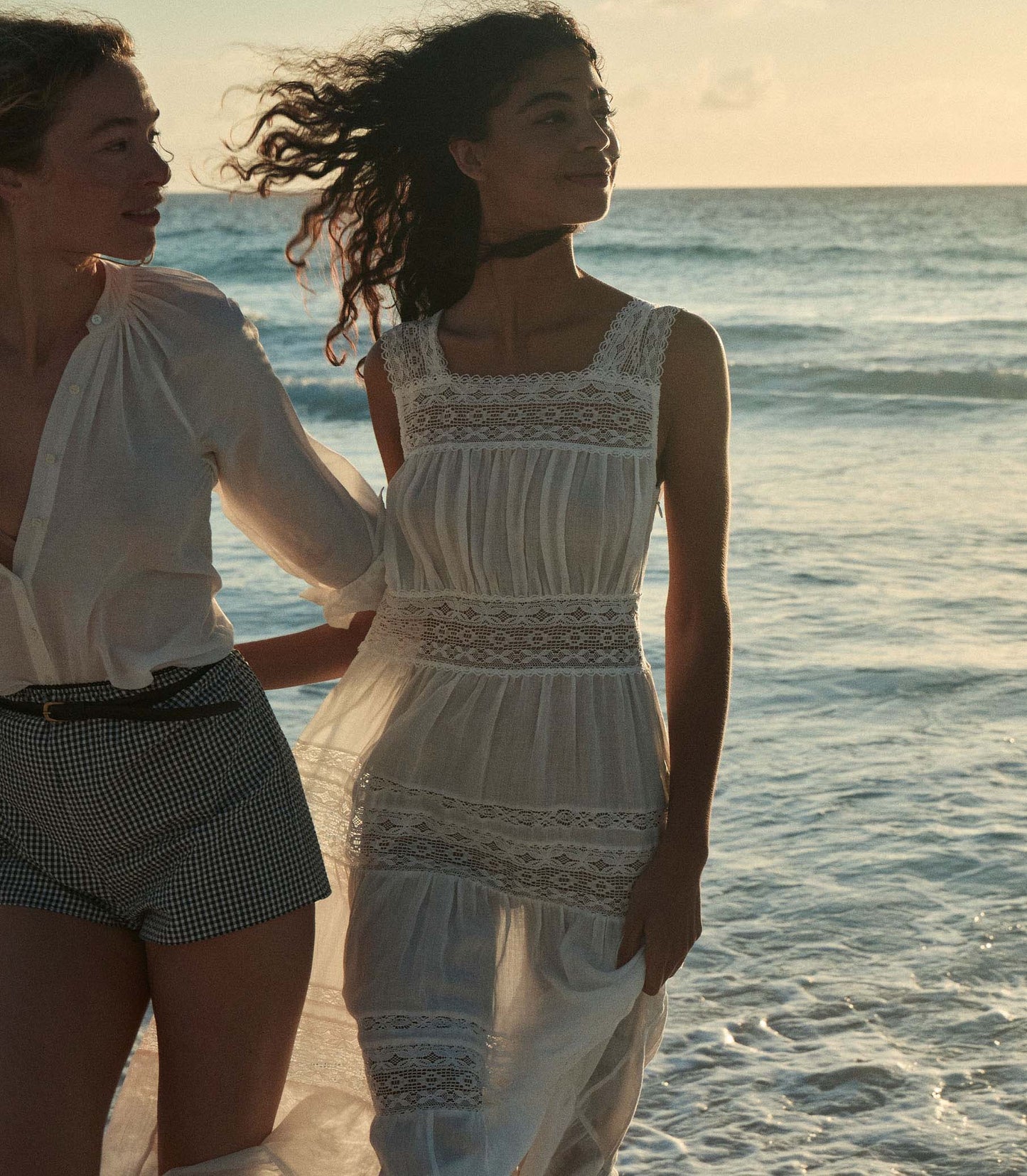 Rocio is wearing a long white sleeveless dress as she walks through the beach.