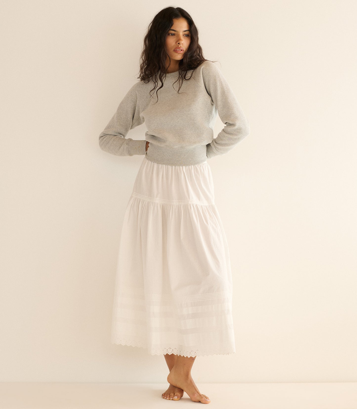 Woman wearing a gray sweater and white skirt against a plain background