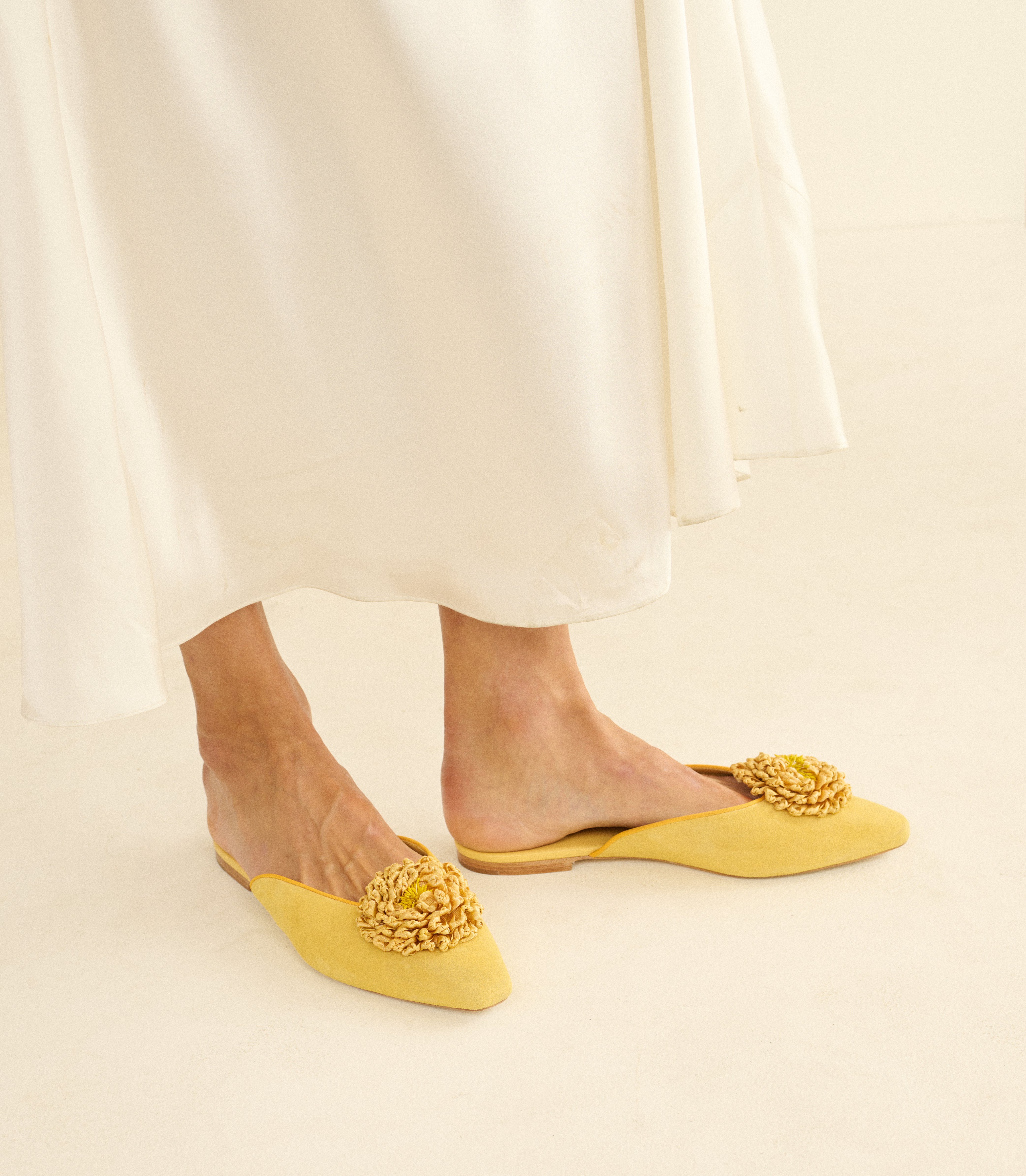 Yellow flats with floral details worn with a white skirt on a light background