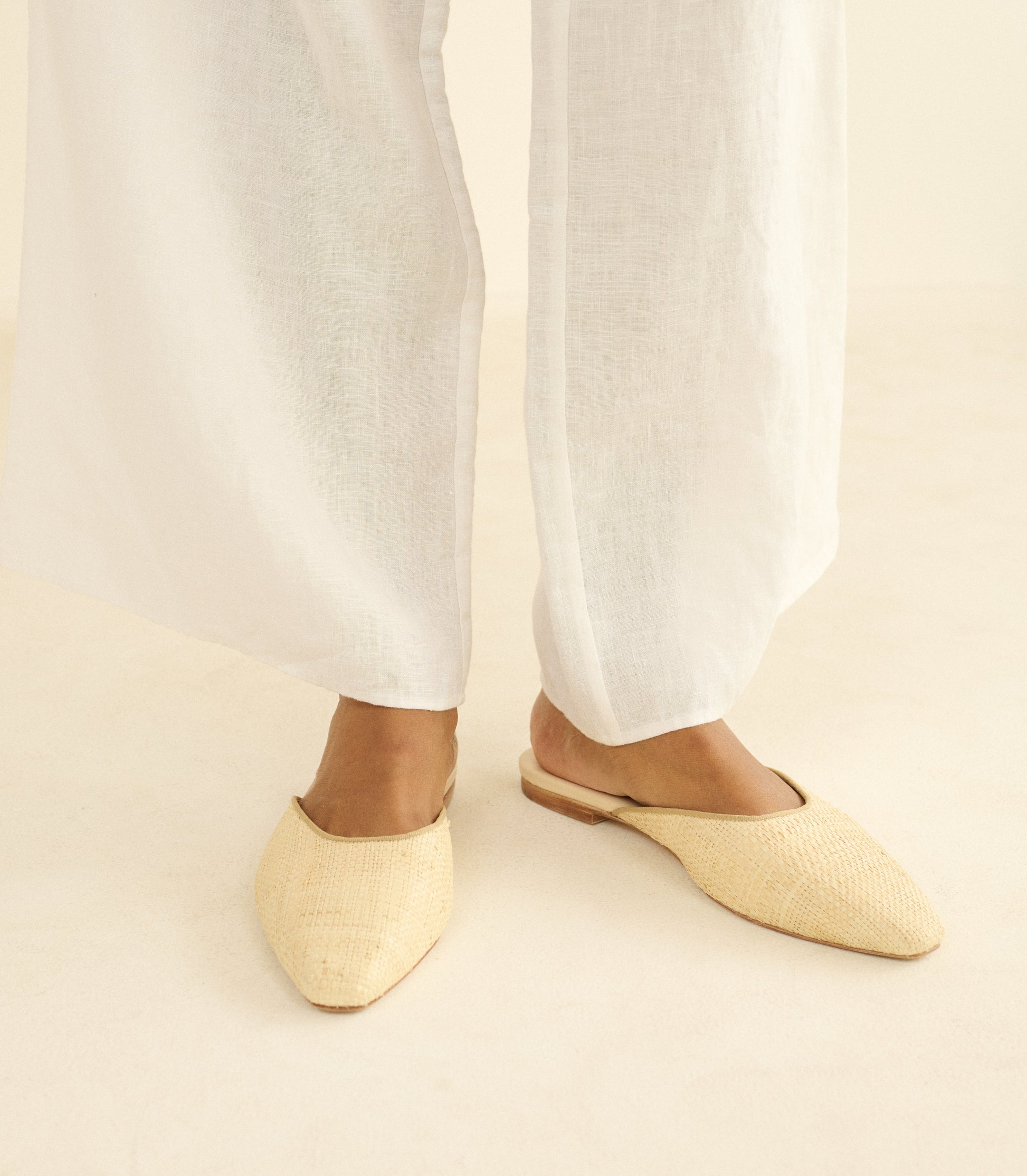 Person wearing beige woven flats with white pants on a neutral background 1
